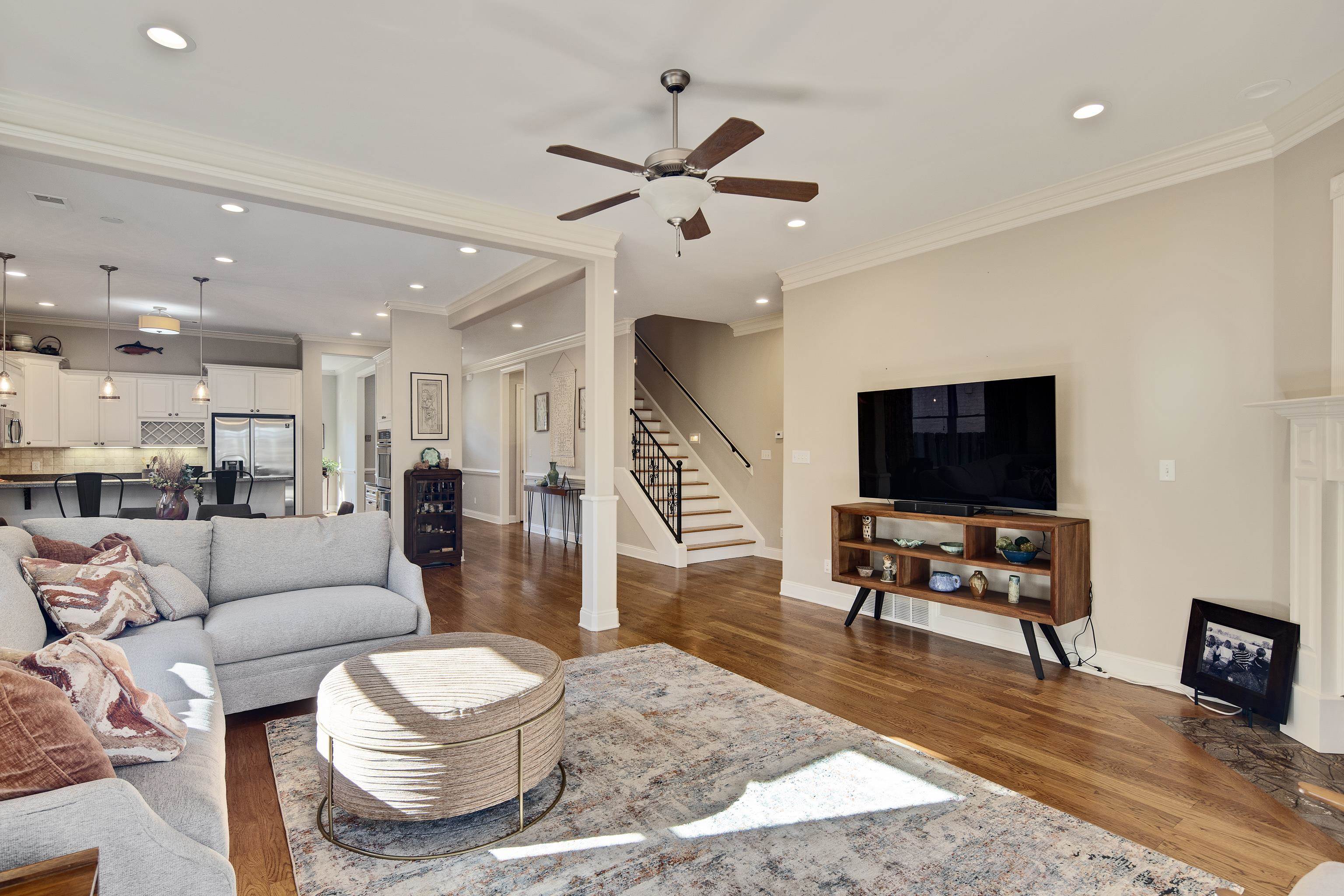 Living room with ceiling fan, dark wood-type flooring, and ornamental molding