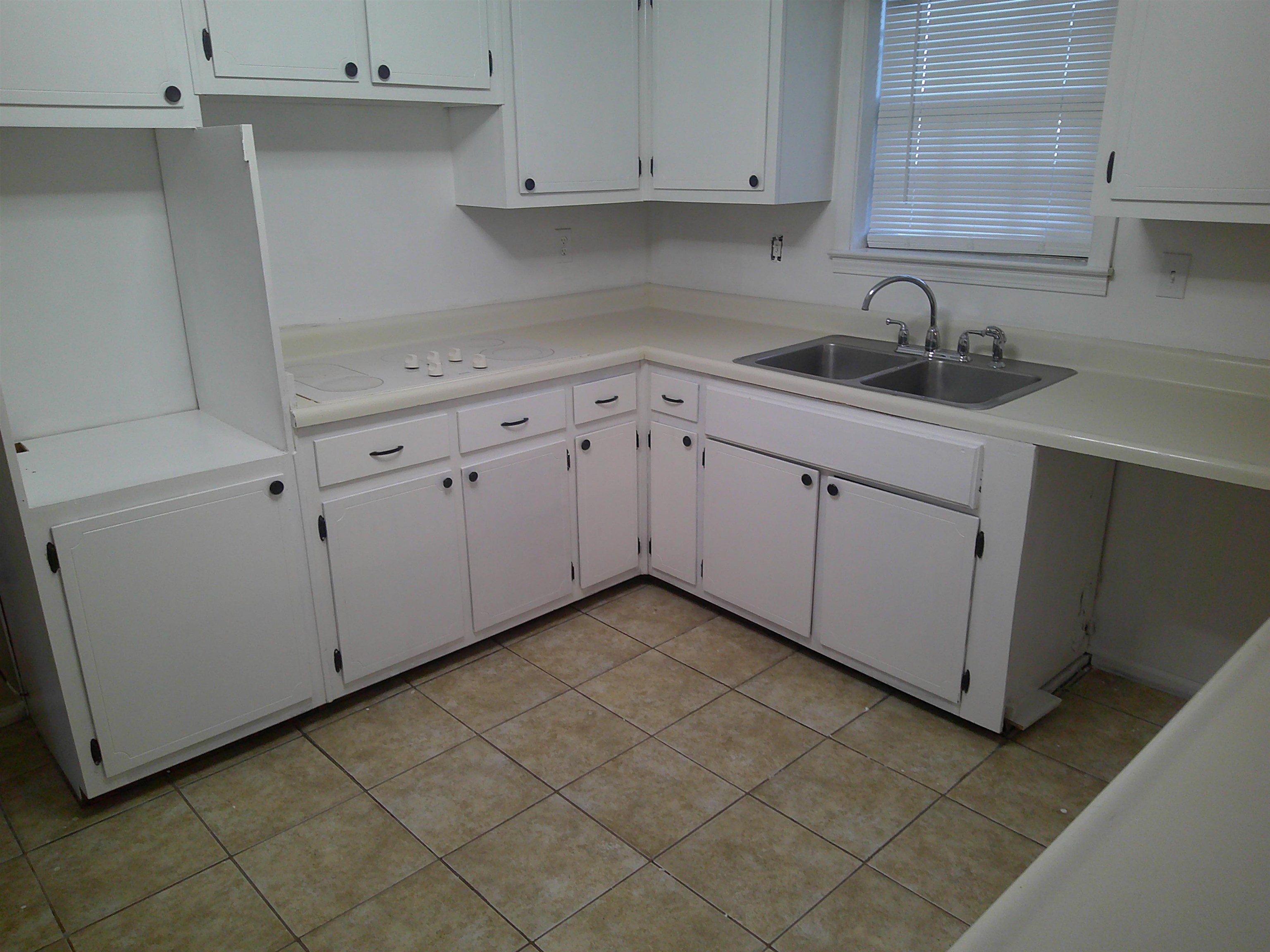 Kitchen with white electric stovetop, light tile patterned floors, white cabinetry, and sink