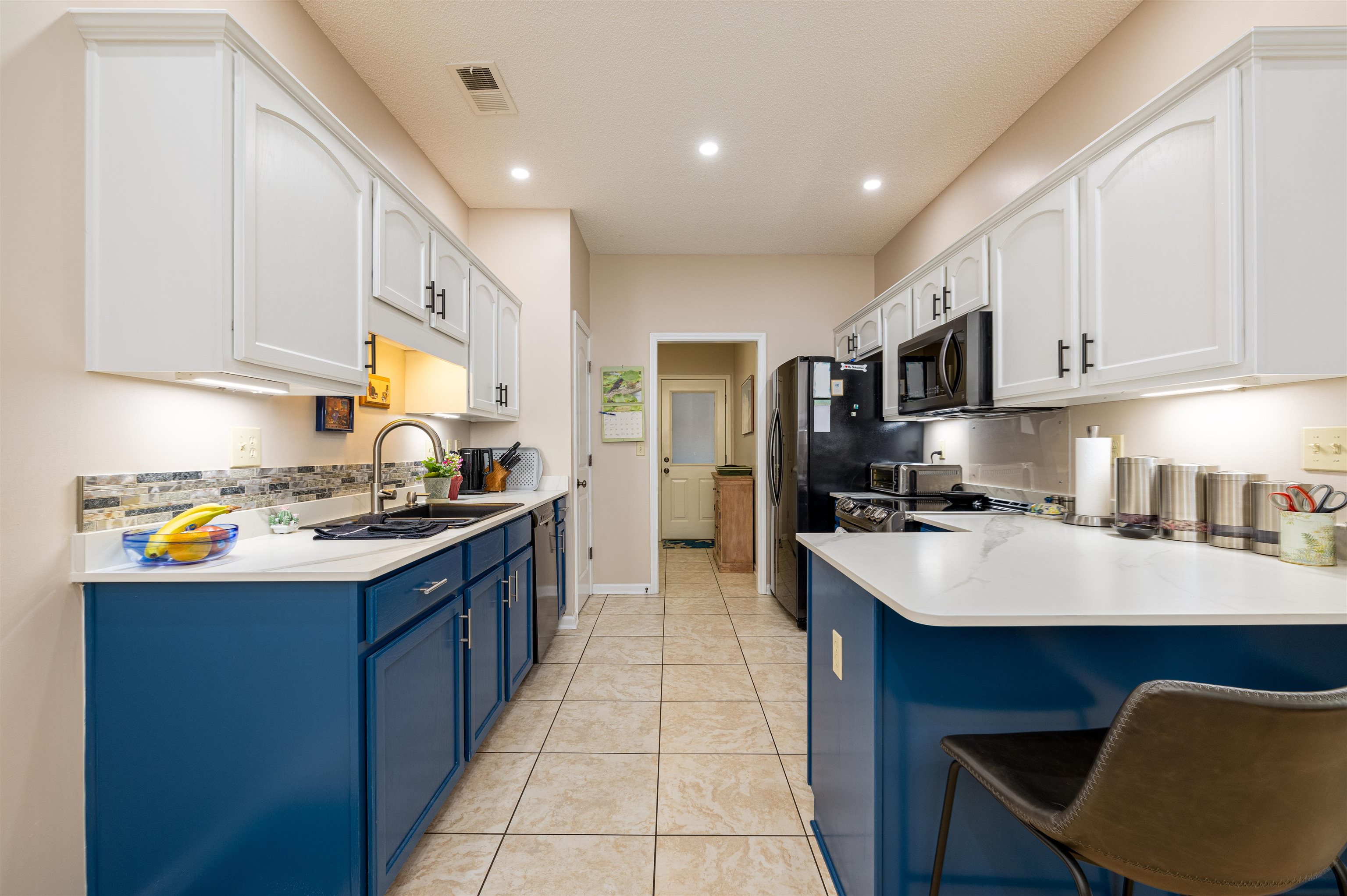 Kitchen with a breakfast bar, blue cabinets, sink, black appliances, and white cabinetry