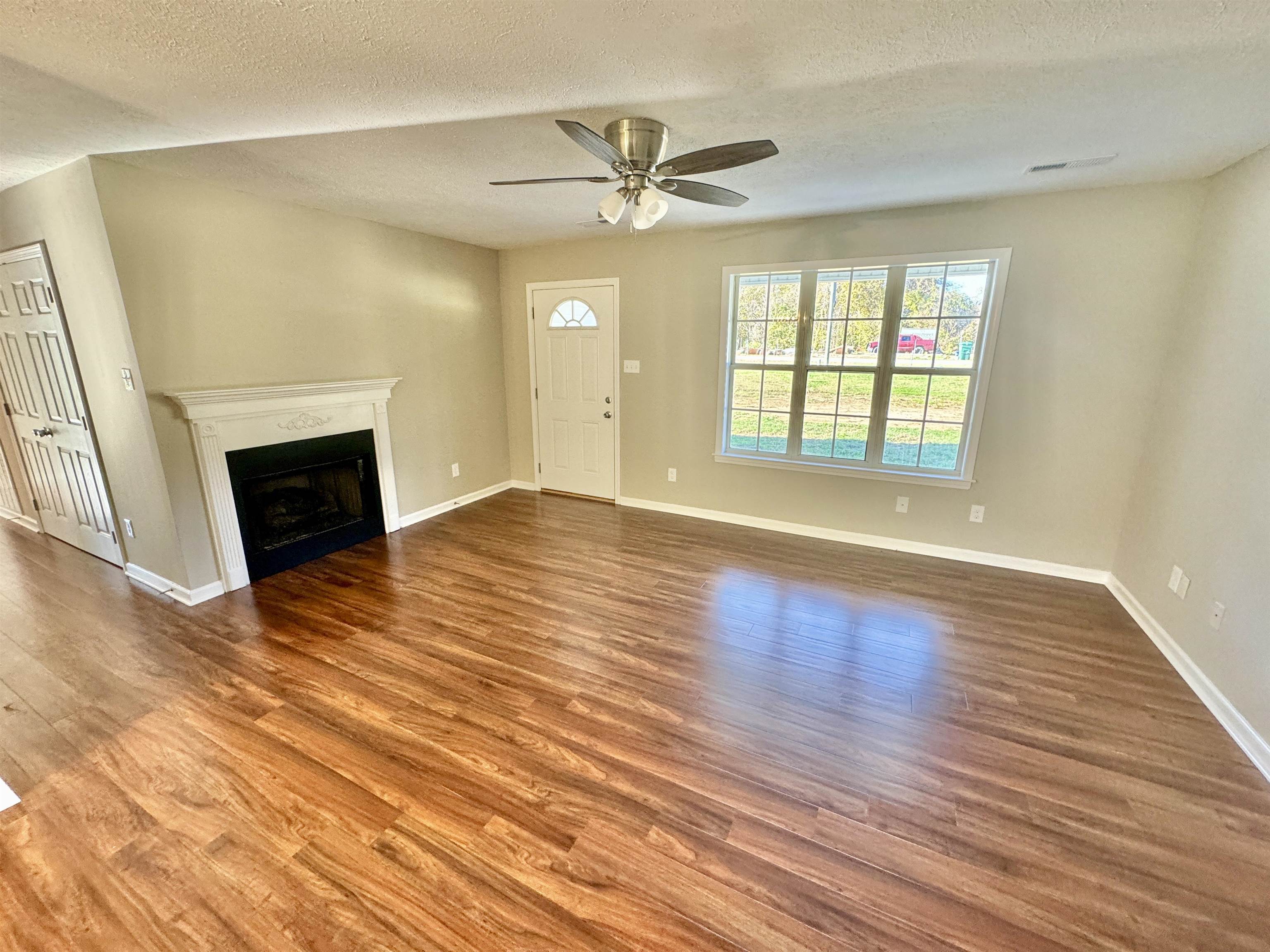 Unfurnished living room featuring hardwood / wood-style flooring, ceiling fan, and a textured ceiling