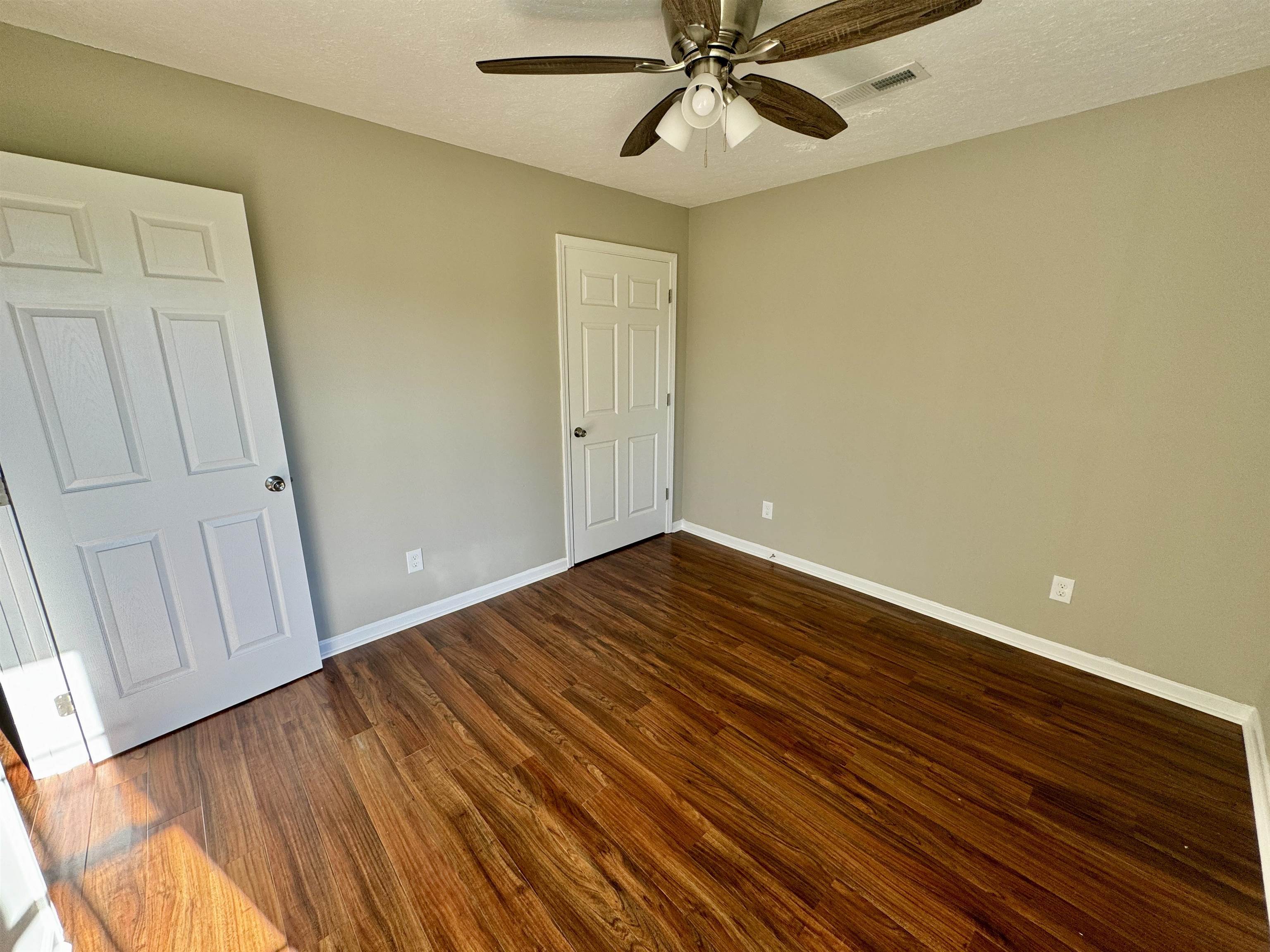 Unfurnished bedroom with a textured ceiling, dark hardwood / wood-style flooring, and ceiling fan