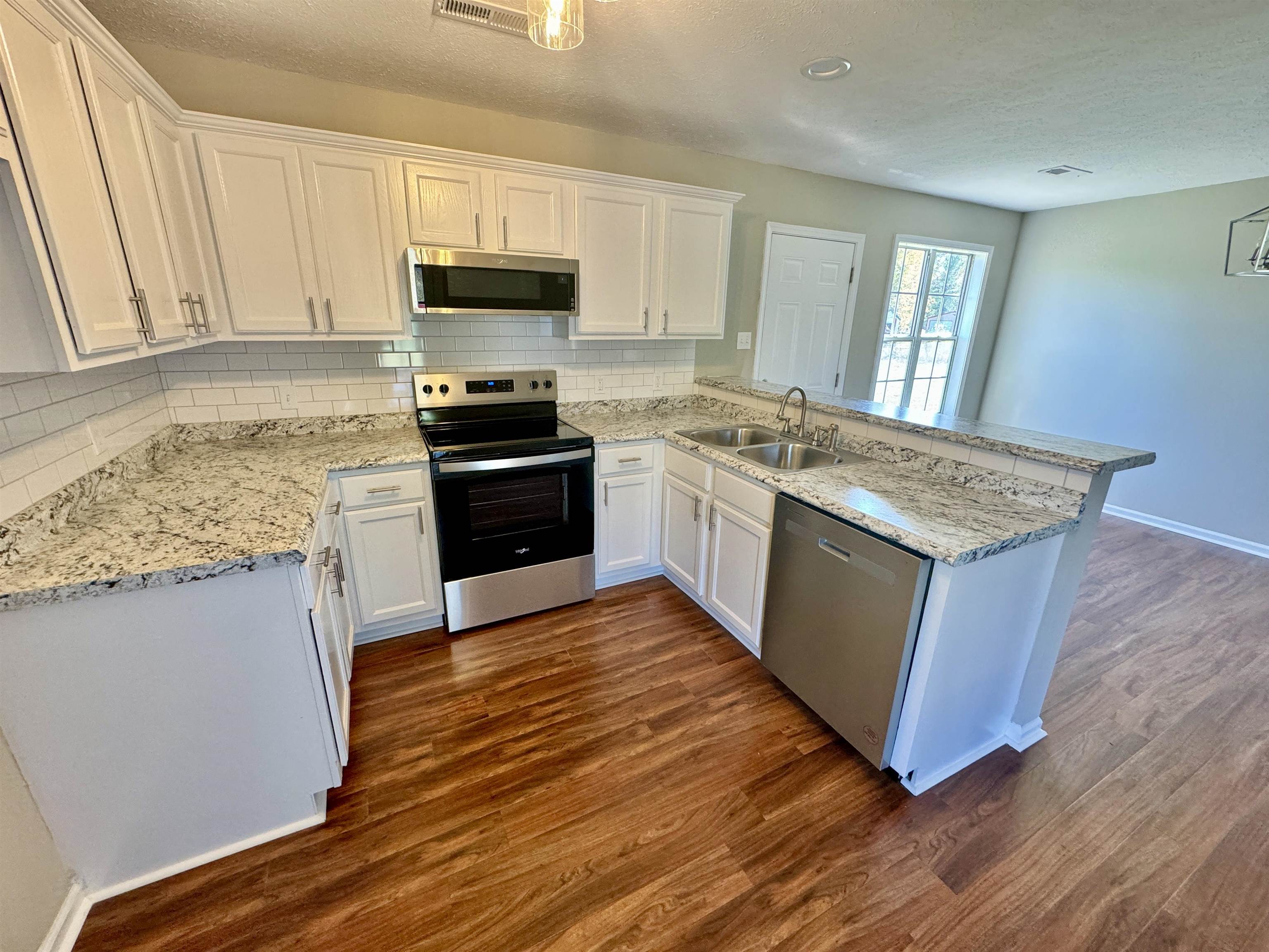 Kitchen featuring kitchen peninsula, sink, appliances with stainless steel finishes, dark hardwood / wood-style flooring, and white cabinetry