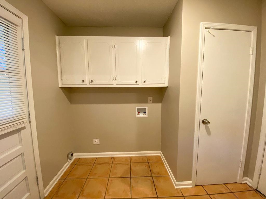 Clothes washing area featuring hookup for a washing machine, light tile patterned flooring, and cabinets