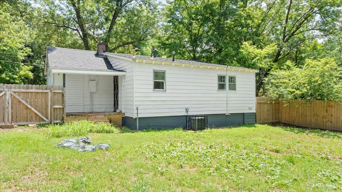 Back of property with central air condition unit and a lawn