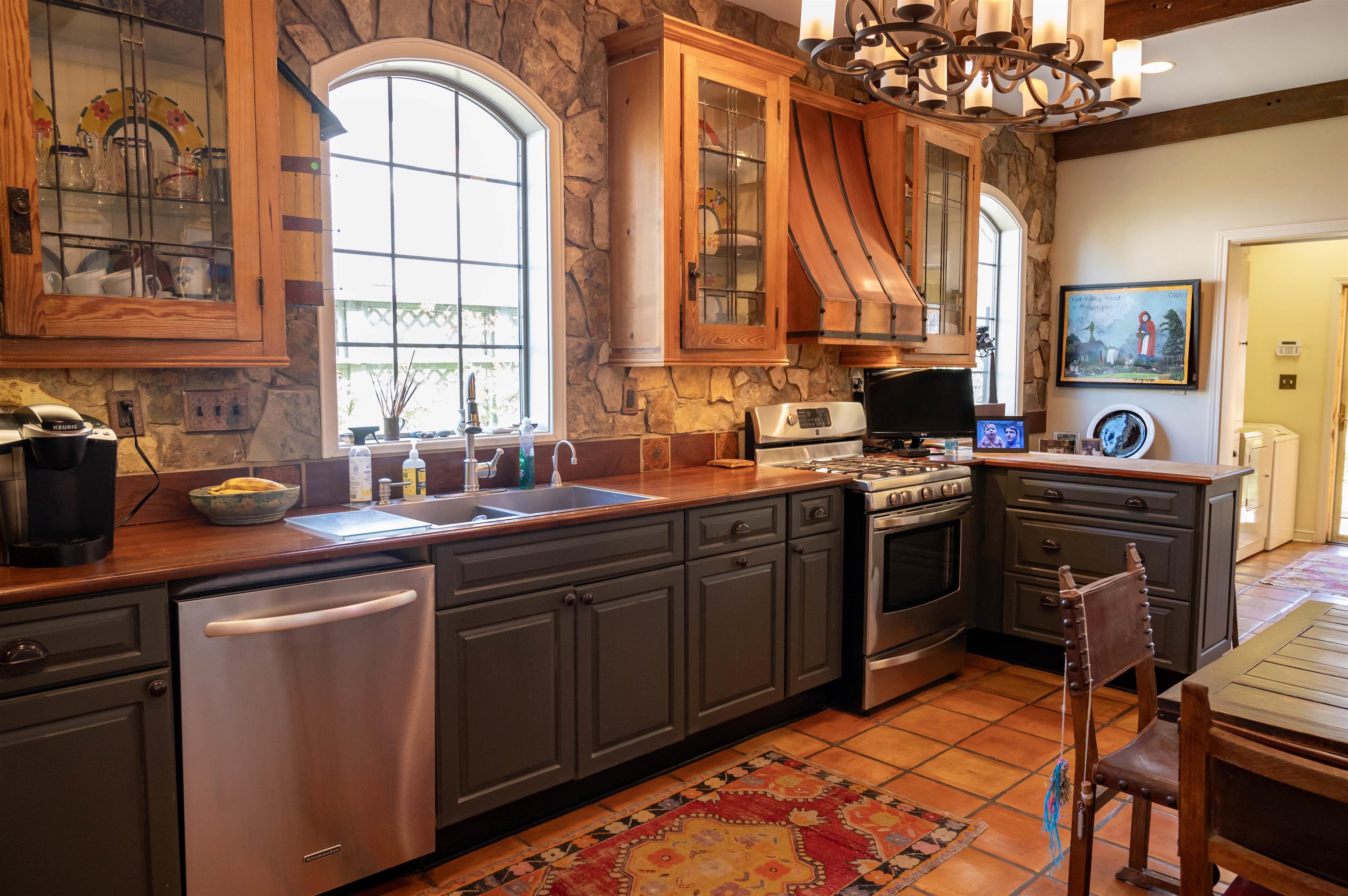 This shot showcases the custom kitchen cabinets with leaded glass doors and lovely window over the kitchen sink with a view of beautiful and fragrant roses.