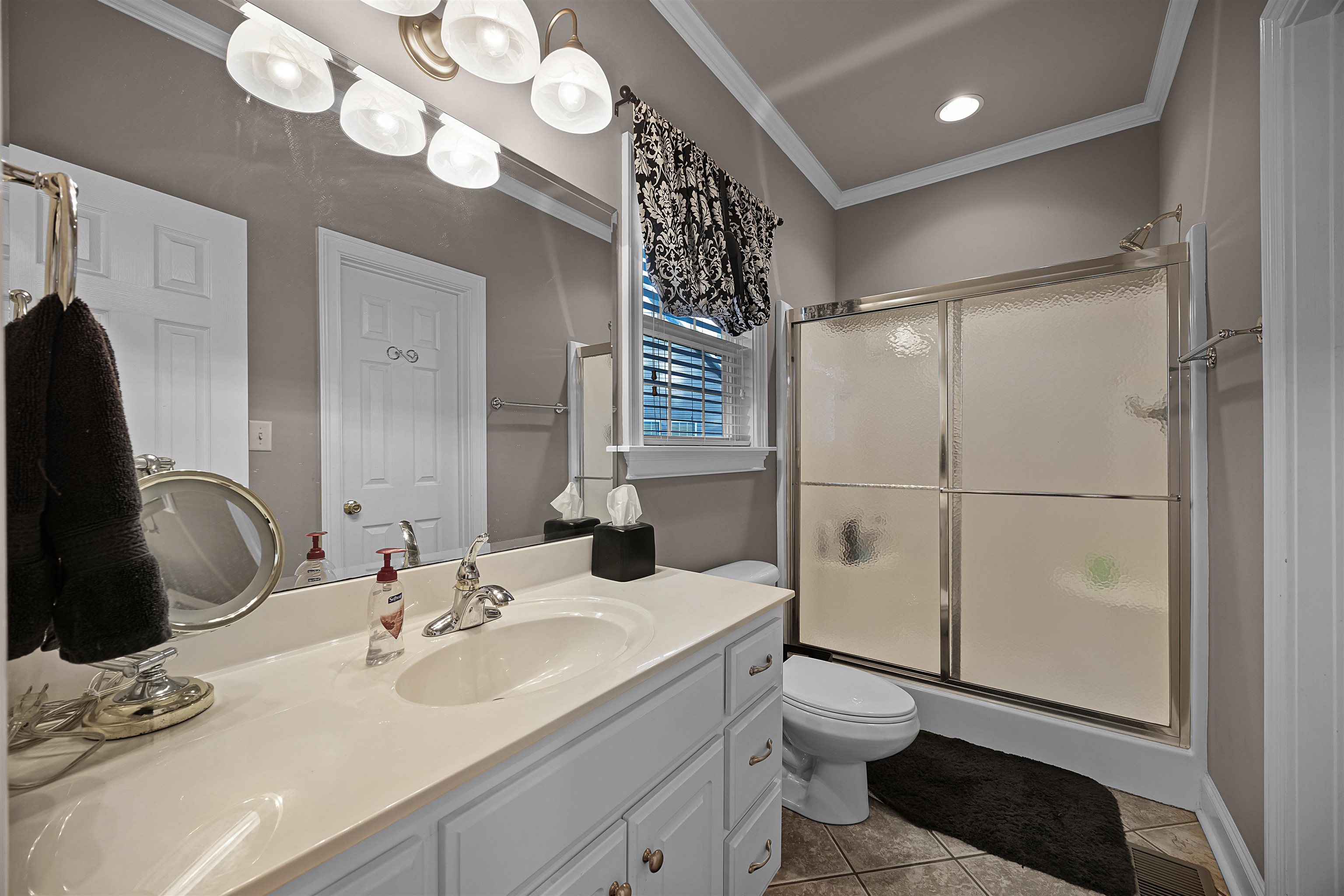 Bathroom featuring vanity, a shower with door, tile patterned floors, toilet, and ornamental molding