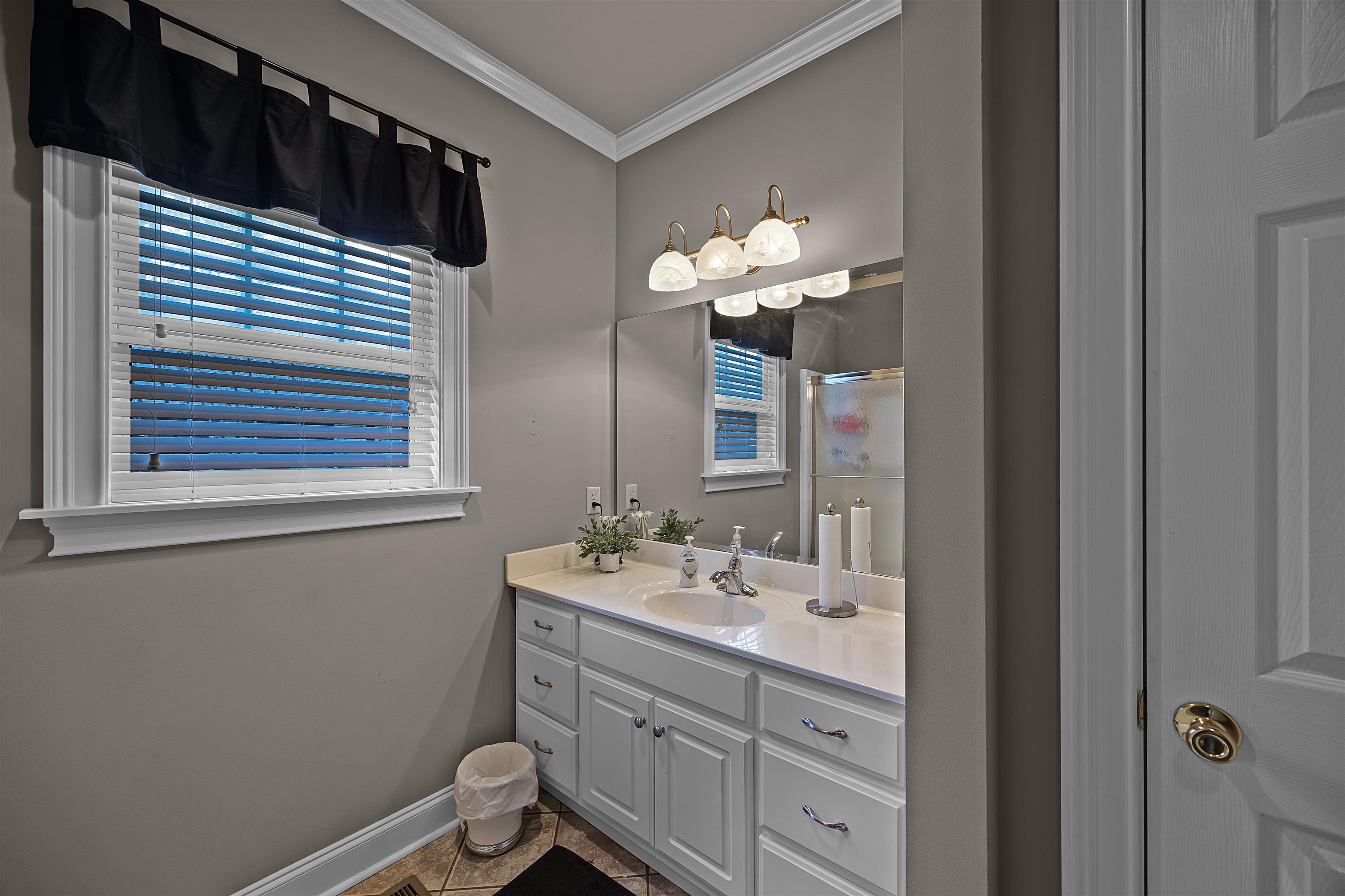 Bathroom featuring tile patterned flooring, vanity, a shower with door, and crown molding