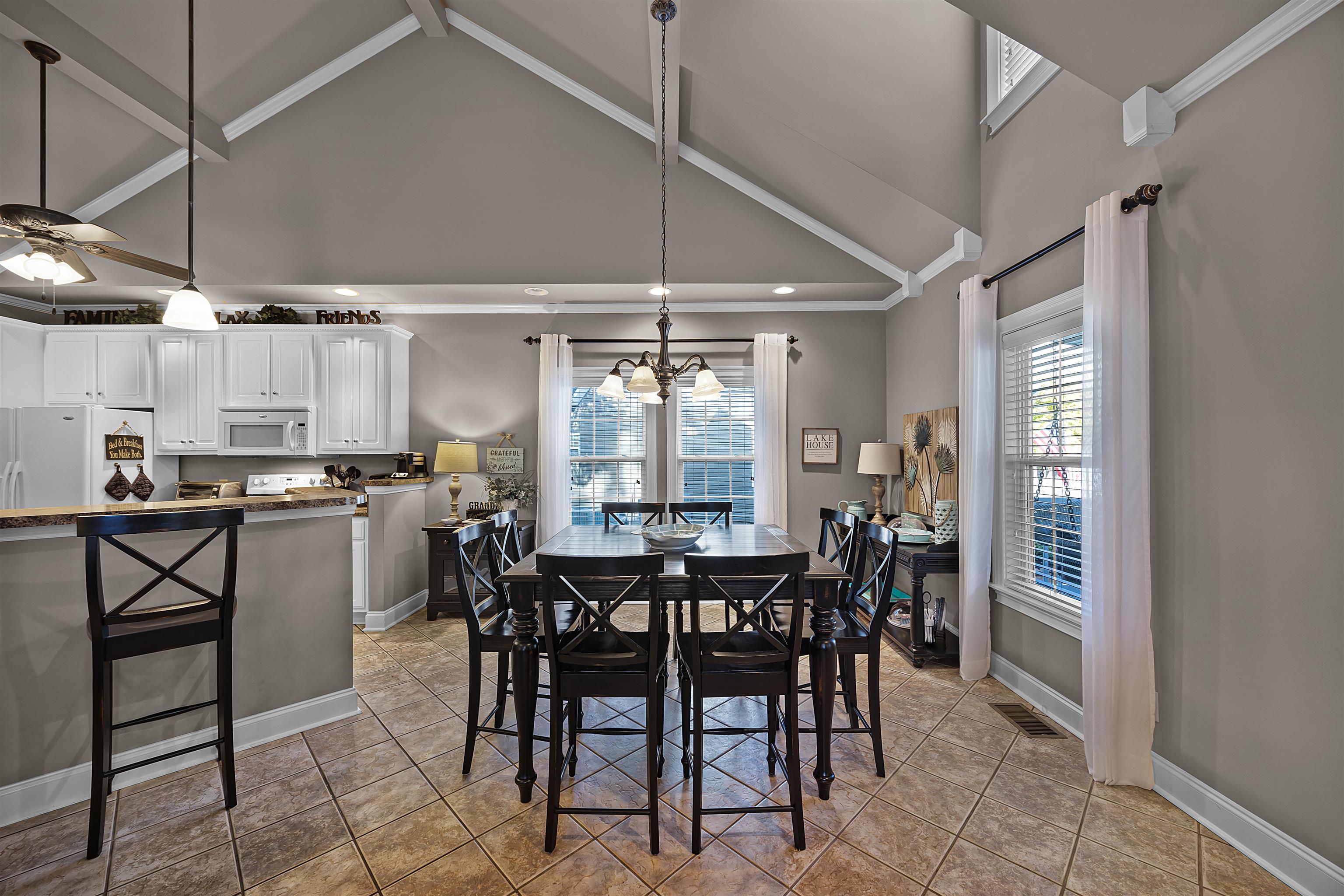 Tiled dining area featuring beamed ceiling, ceiling fan with notable chandelier, and high vaulted ceiling