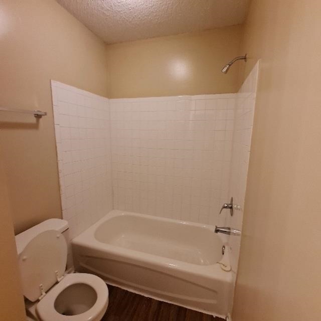 Bathroom with shower / bathing tub combination, a textured ceiling, and toilet