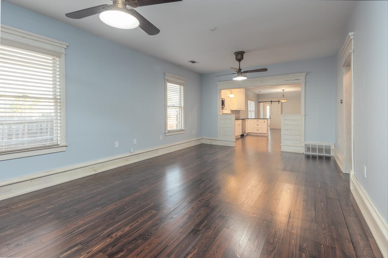 Unfurnished living room featuring ceiling fan with notable chandelier and dark wood-type flooring