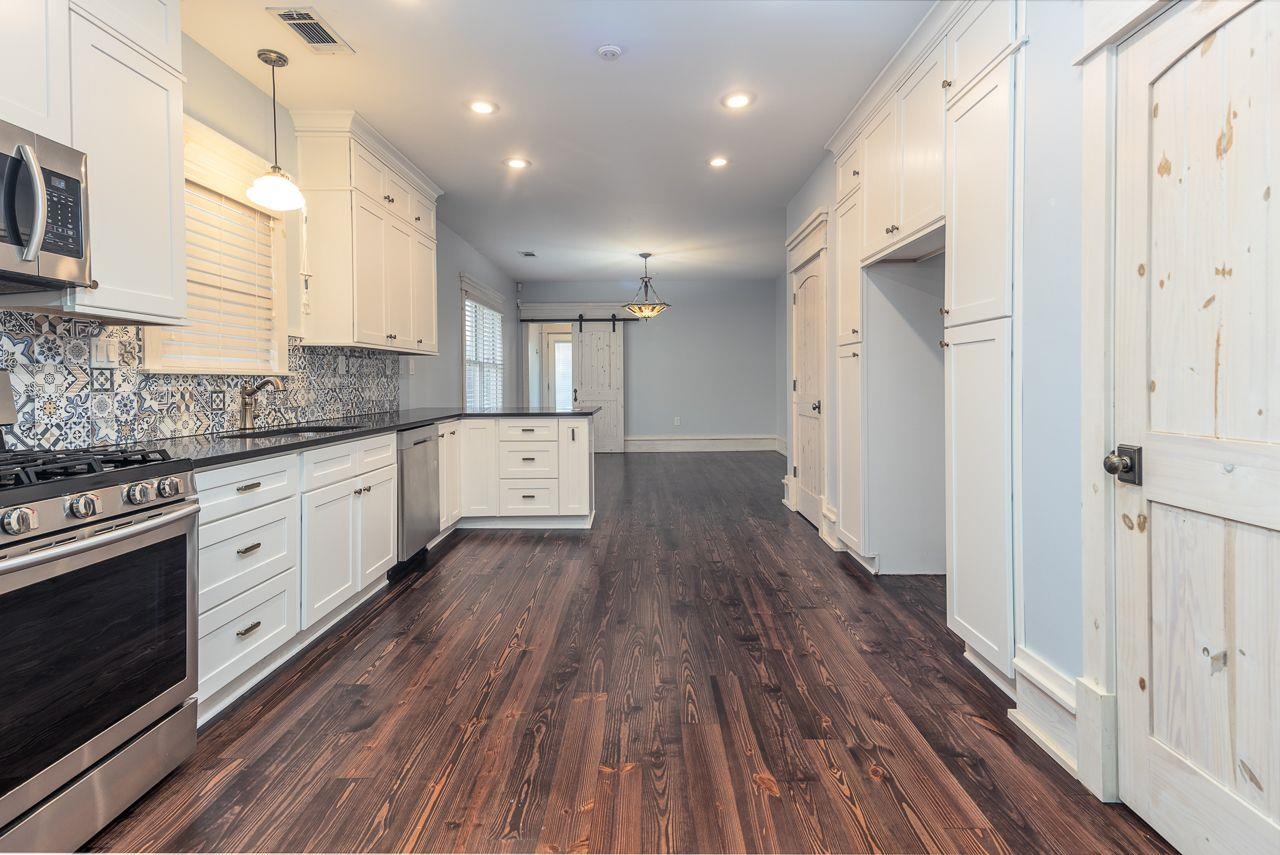 Kitchen featuring appliances with stainless steel finishes, dark wood-type flooring, a barn door, decorative light fixtures, and white cabinetry