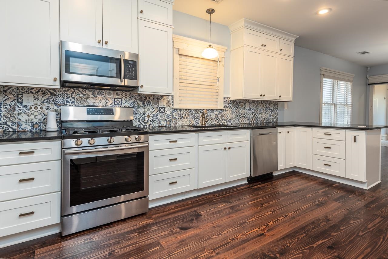 Kitchen with sink, kitchen peninsula, appliances with stainless steel finishes, dark hardwood / wood-style floors, and decorative light fixtures