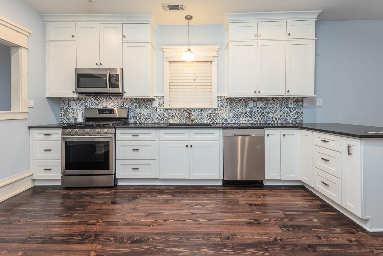 Kitchen with sink, hanging light fixtures, dark hardwood / wood-style floors, appliances with stainless steel finishes, and white cabinetry