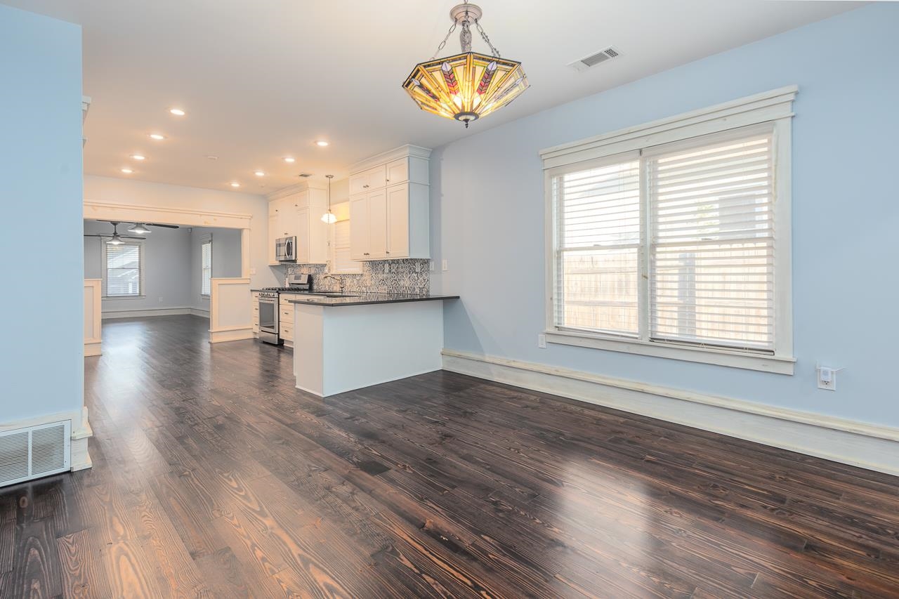 Kitchen featuring tasteful backsplash, appliances with stainless steel finishes, hanging light fixtures, white cabinets, and dark wood-type flooring