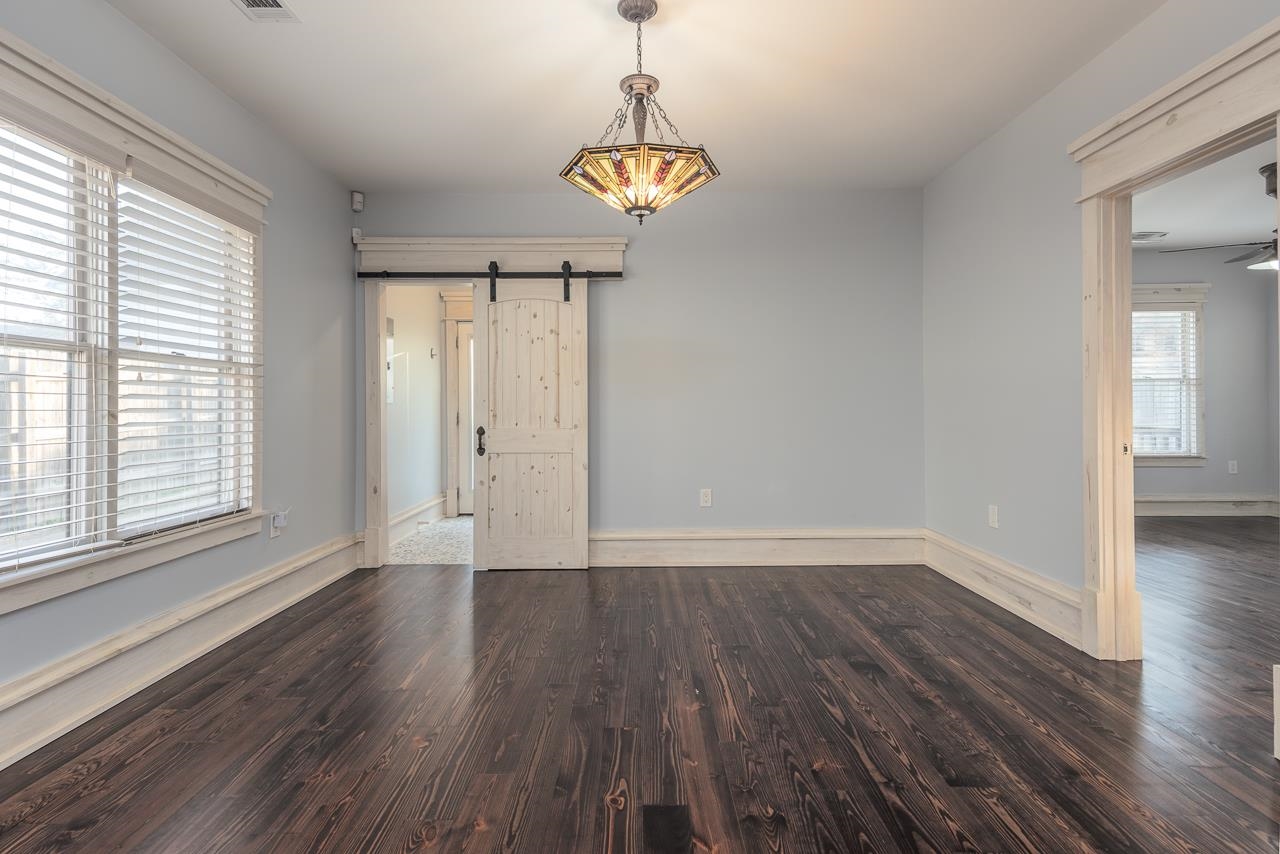 Unfurnished room featuring ceiling fan, a barn door, and dark hardwood / wood-style floors