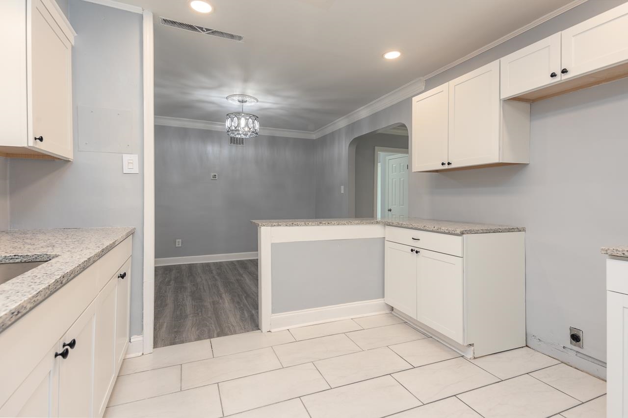 Kitchen with light hardwood / wood-style floors, white cabinetry, crown molding, and light stone counters