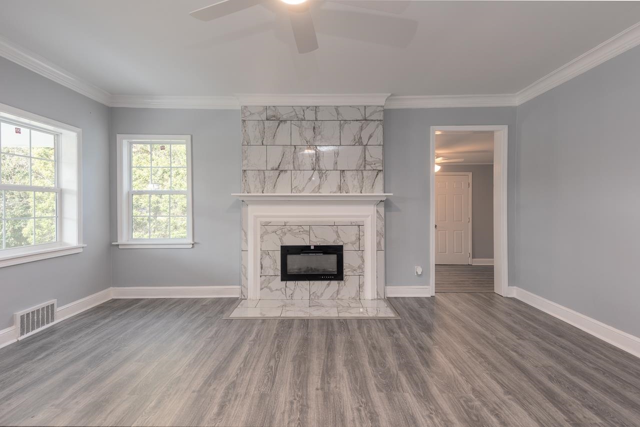 Unfurnished living room with crown molding, a high end fireplace, wood-type flooring, and ceiling fan