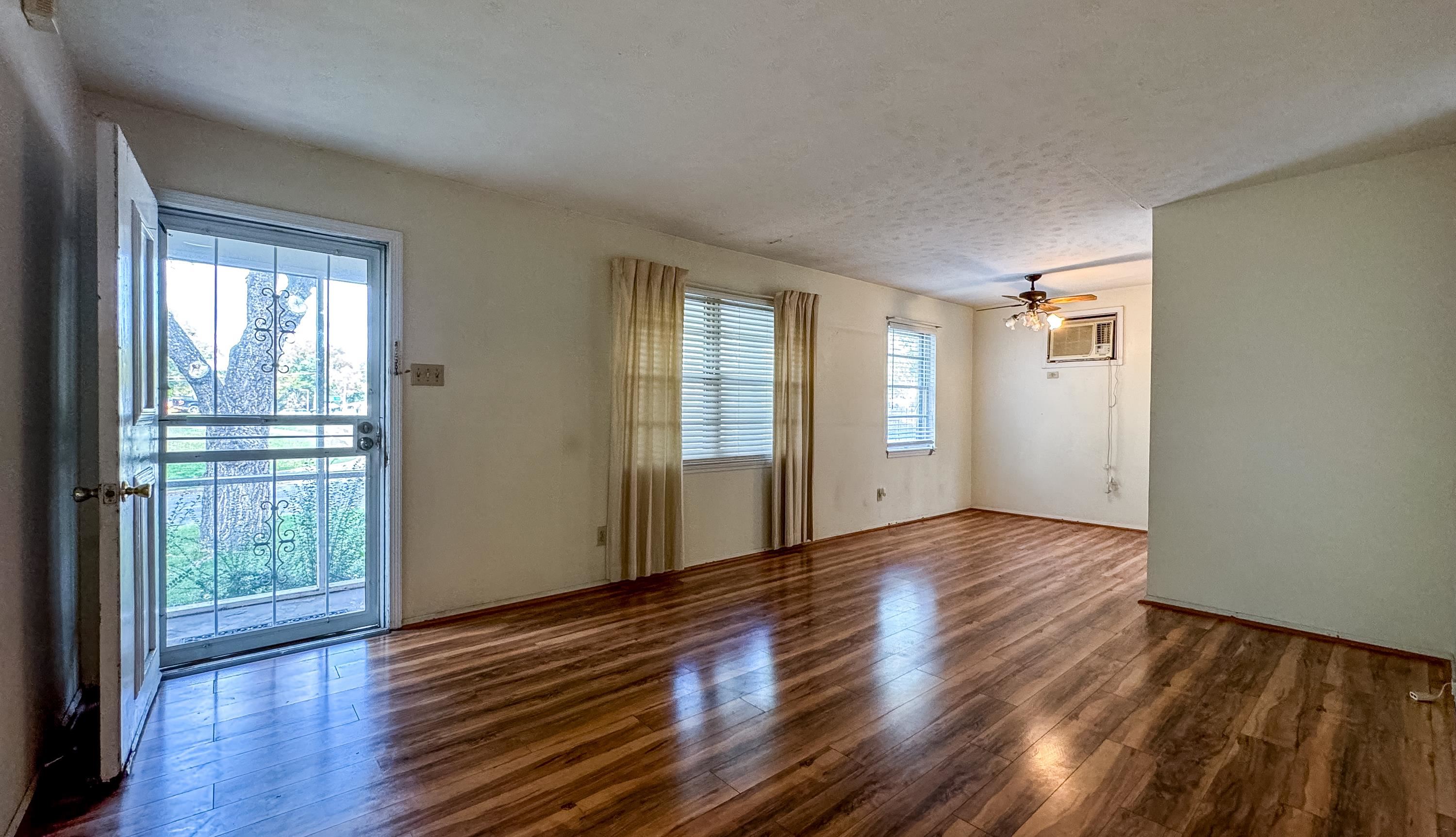 Unfurnished room featuring a textured ceiling, ceiling fan, dark wood-type flooring, and a wall mounted air conditioner