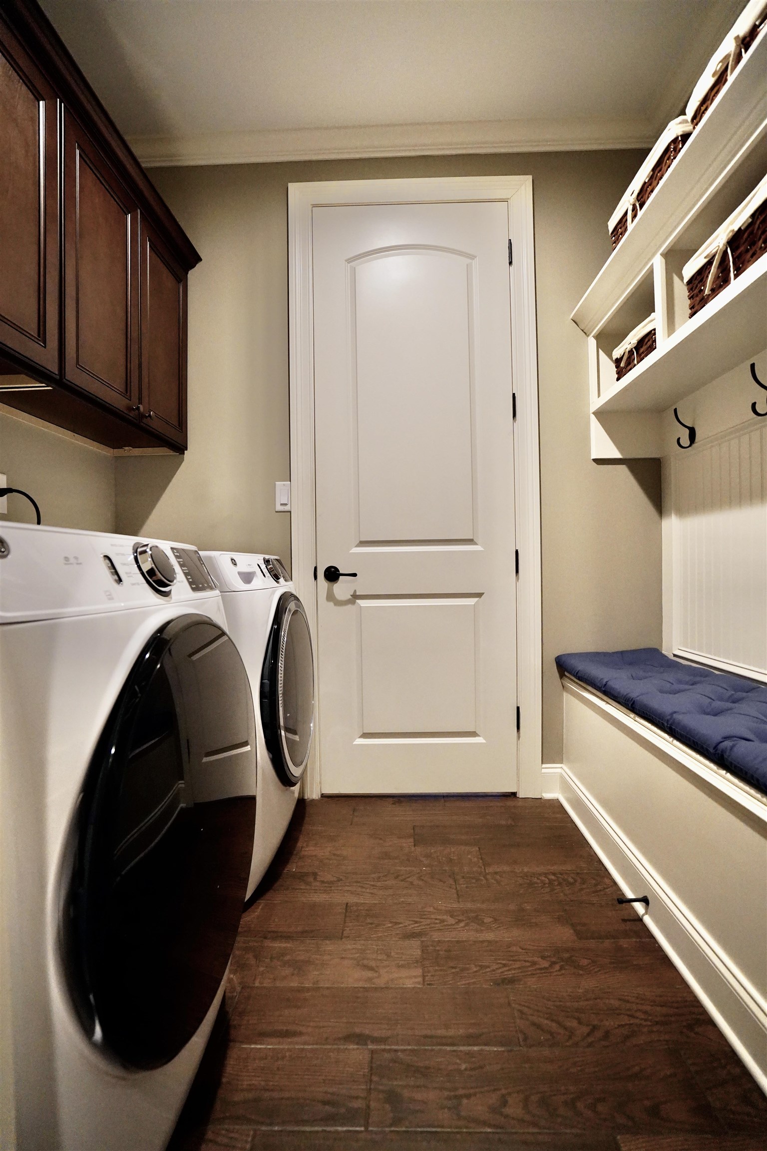 Clothes washing area with ornamental molding, separate washer and dryer, dark wood-type flooring, and cabinets