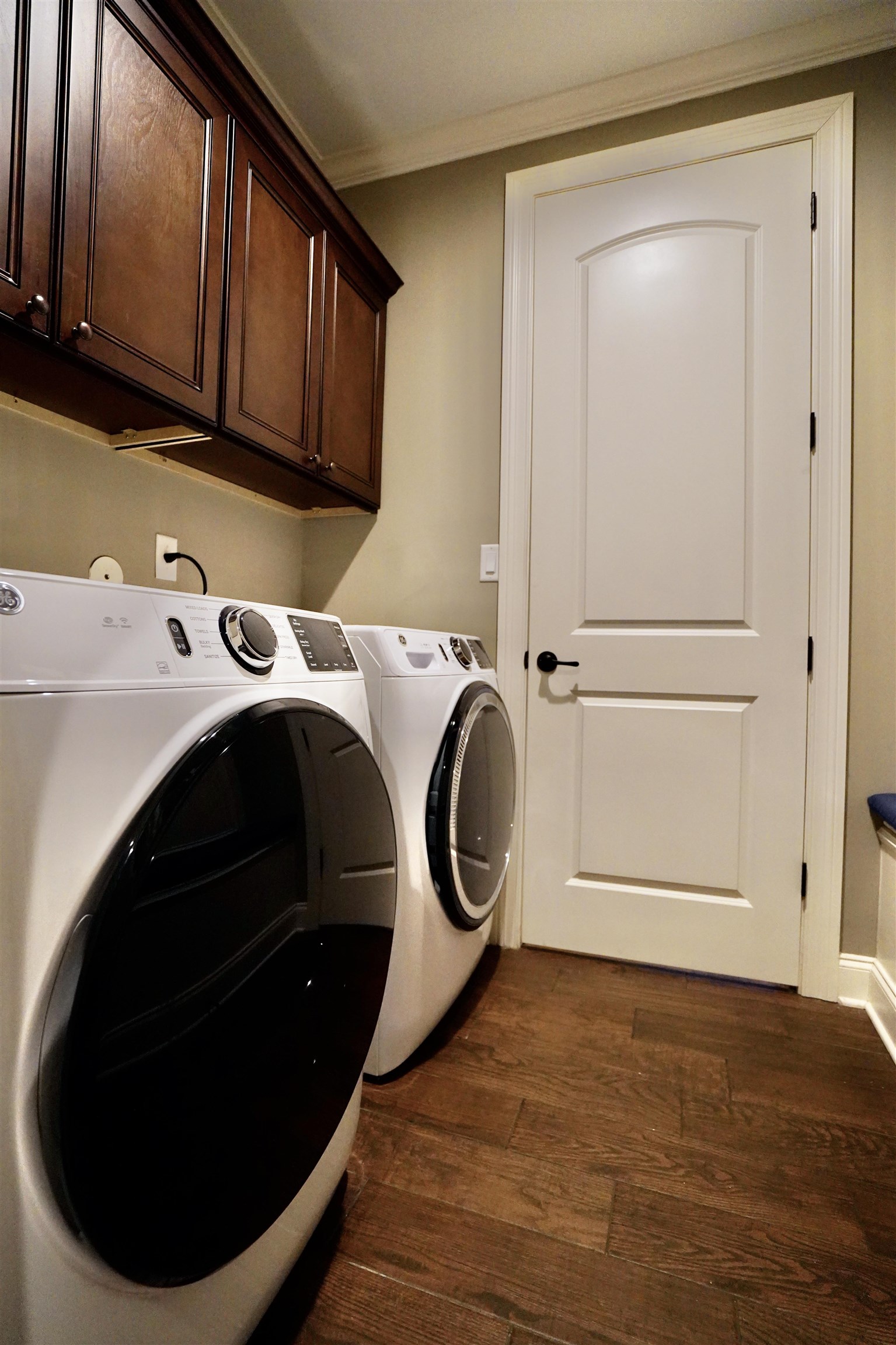 Laundry room with dark wood-type flooring, cabinets, washer and dryer, and ornamental molding