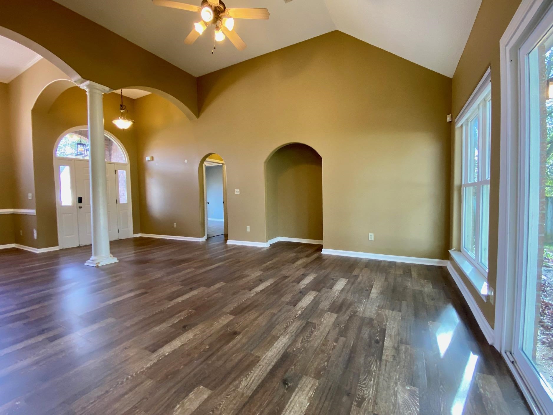 Unfurnished living room featuring ceiling fan, a healthy amount of sunlight, dark wood-type flooring, and decorative columns