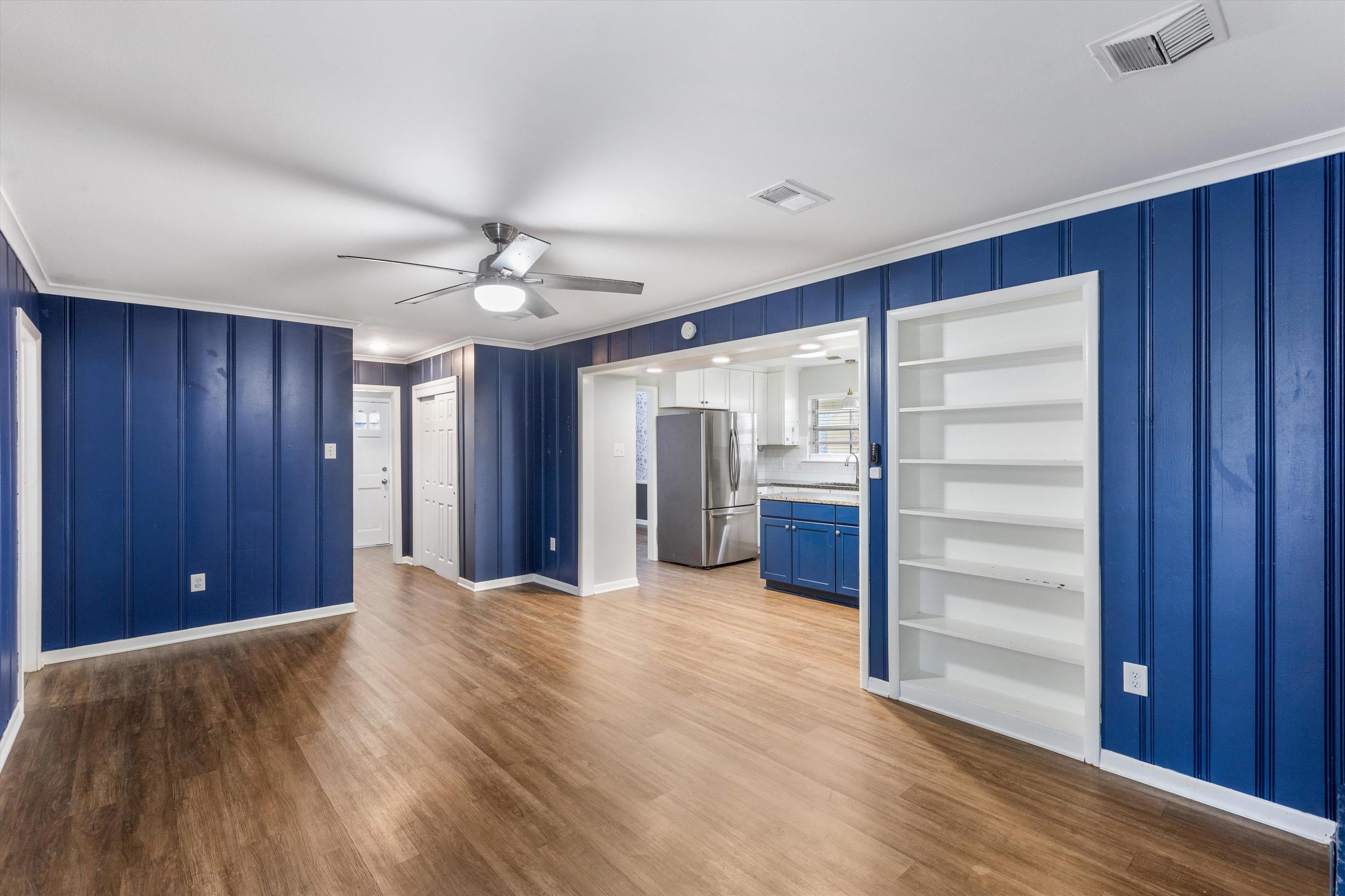 Unfurnished living room featuring hardwood / wood-style floors, built in shelves, crown molding, and ceiling fan