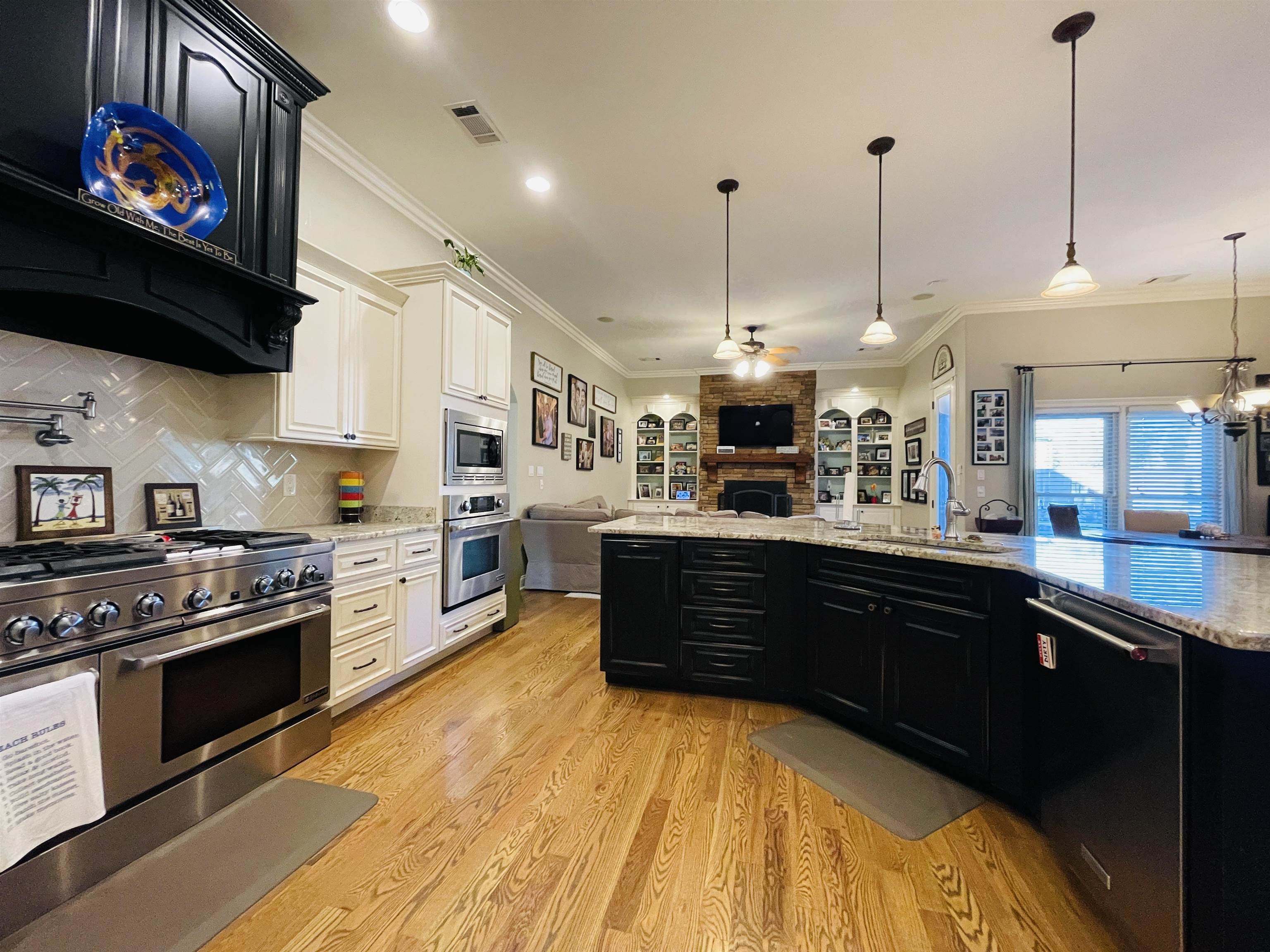 Kitchen with backsplash, ceiling fan with notable chandelier, crown molding, light wood-type flooring, and stainless steel appliances