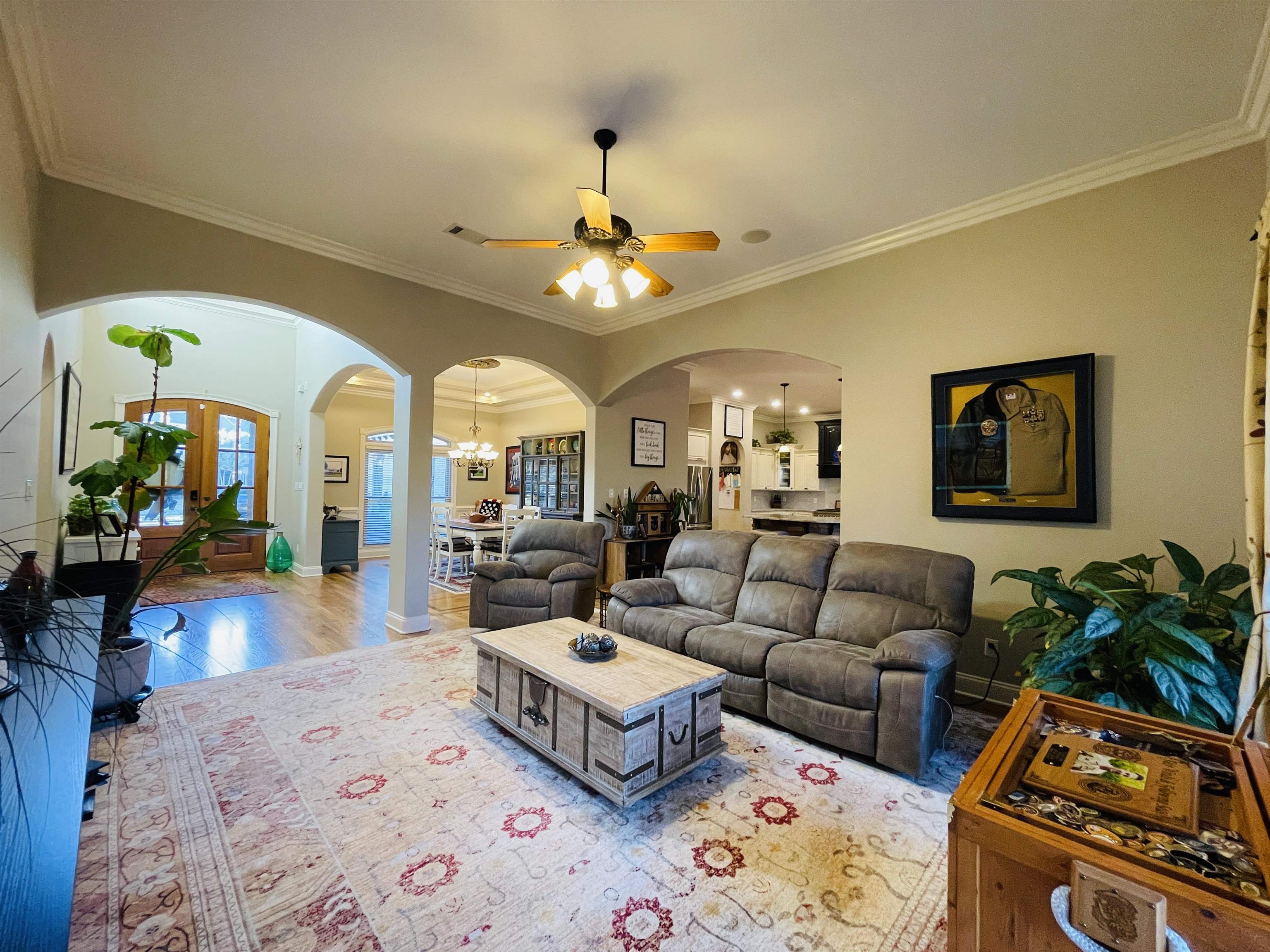 Living room with ceiling fan with notable chandelier, light hardwood / wood-style flooring, and crown molding