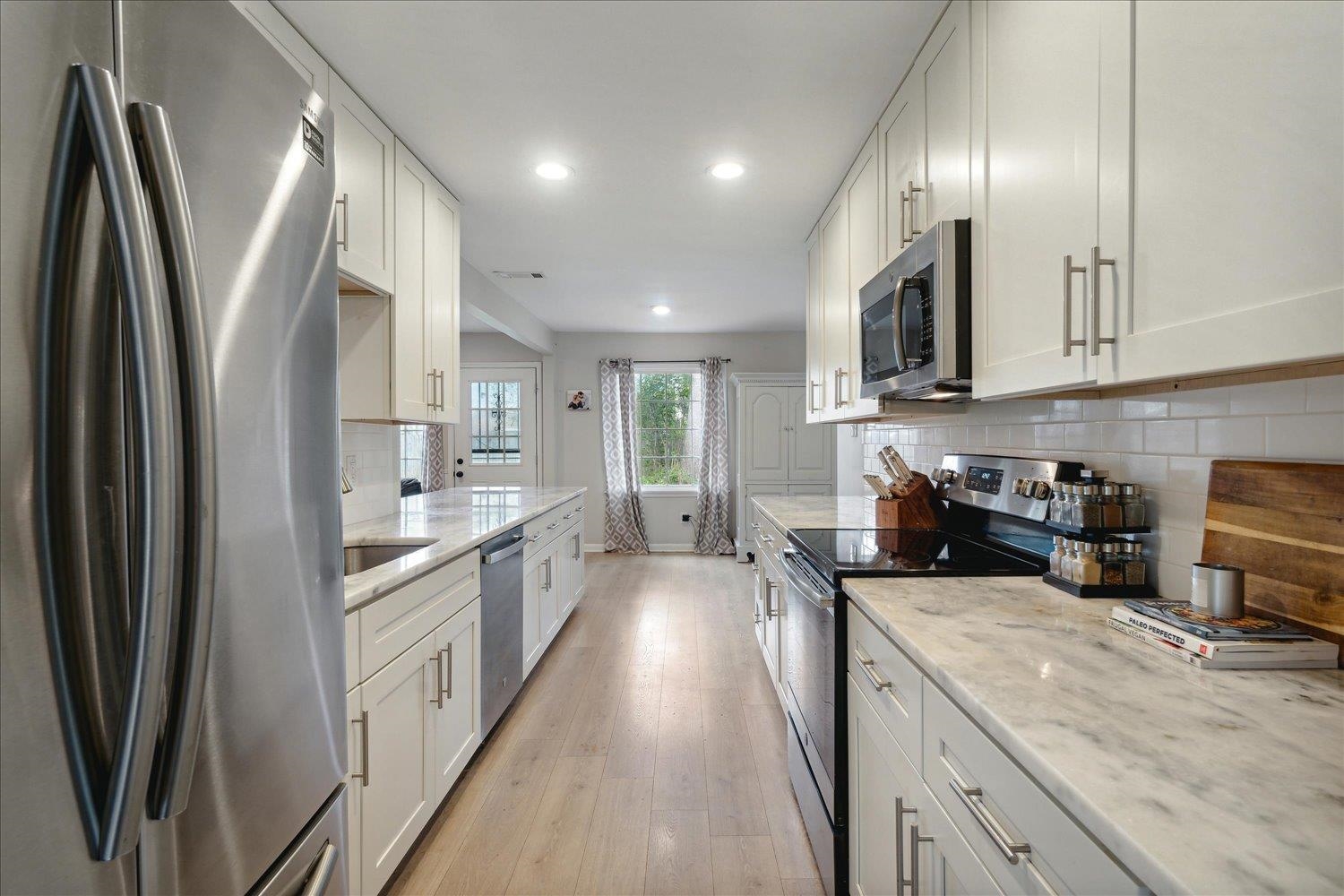 Kitchen featuring light stone countertops, white cabinetry, appliances with stainless steel finishes, and light hardwood / wood-style flooring