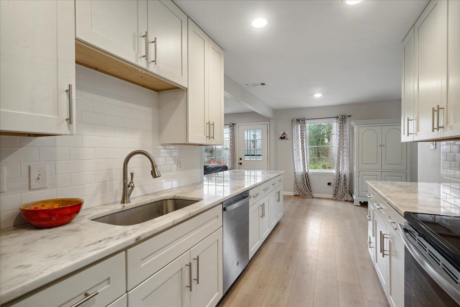 Kitchen with light stone countertops, sink, stainless steel appliances, white cabinets, and light wood-type flooring