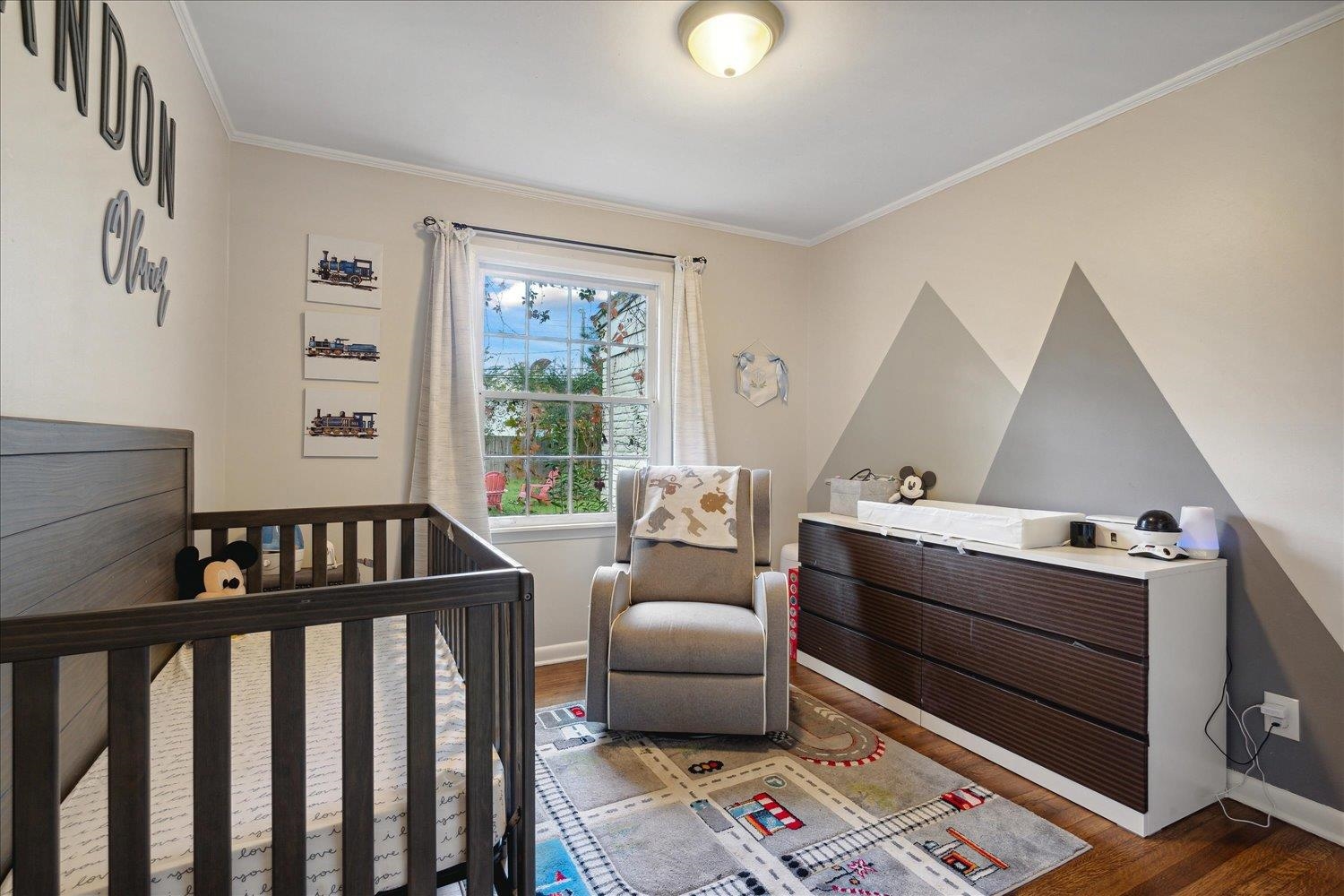 Bedroom with crown molding, a nursery area, and dark wood-type flooring