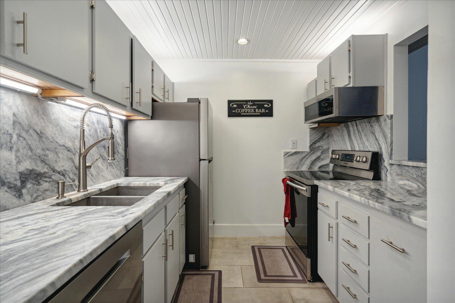 Kitchen with decorative backsplash, appliances with stainless steel finishes, light tile patterned flooring, and sink