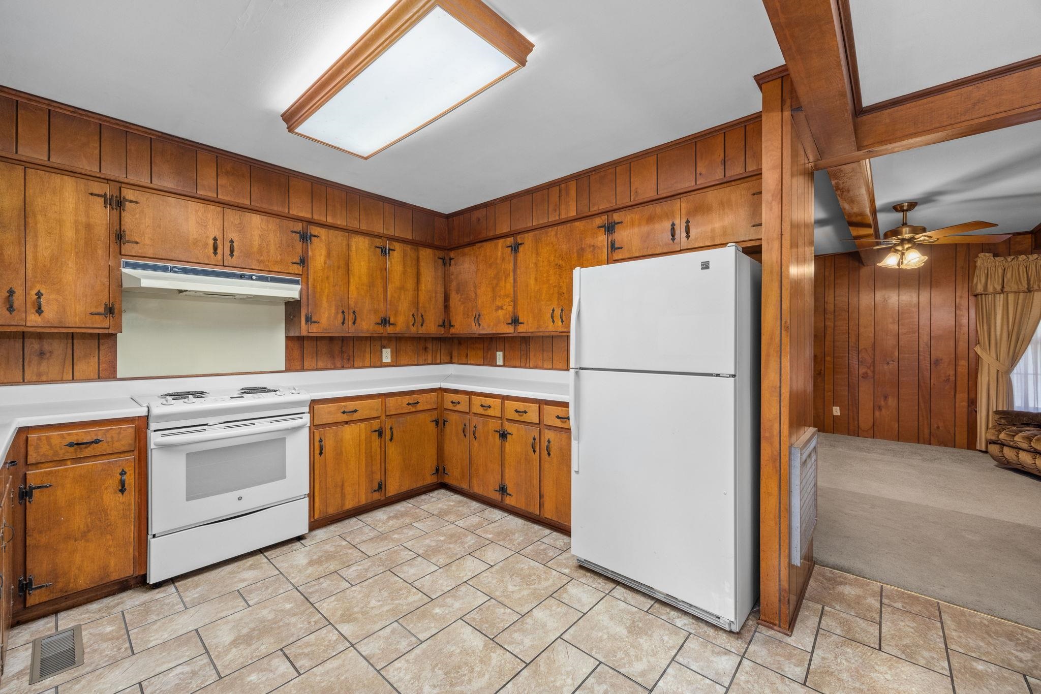 Kitchen featuring ceiling fan, light colored carpet, white appliances, and wooden walls