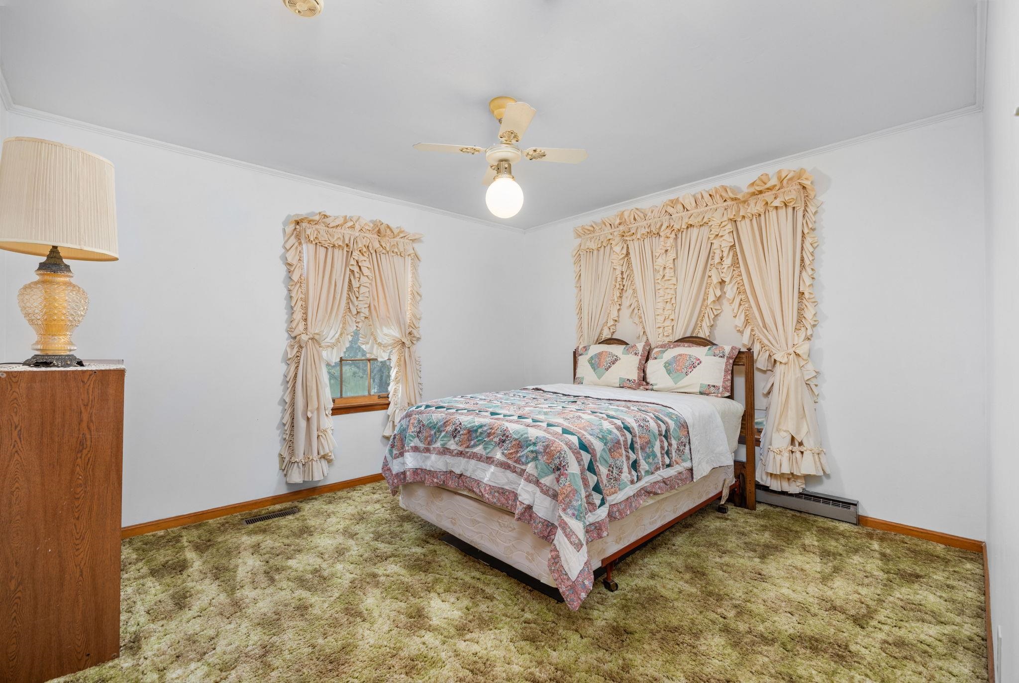 Carpeted bedroom with baseboard heating, ceiling fan, and crown molding