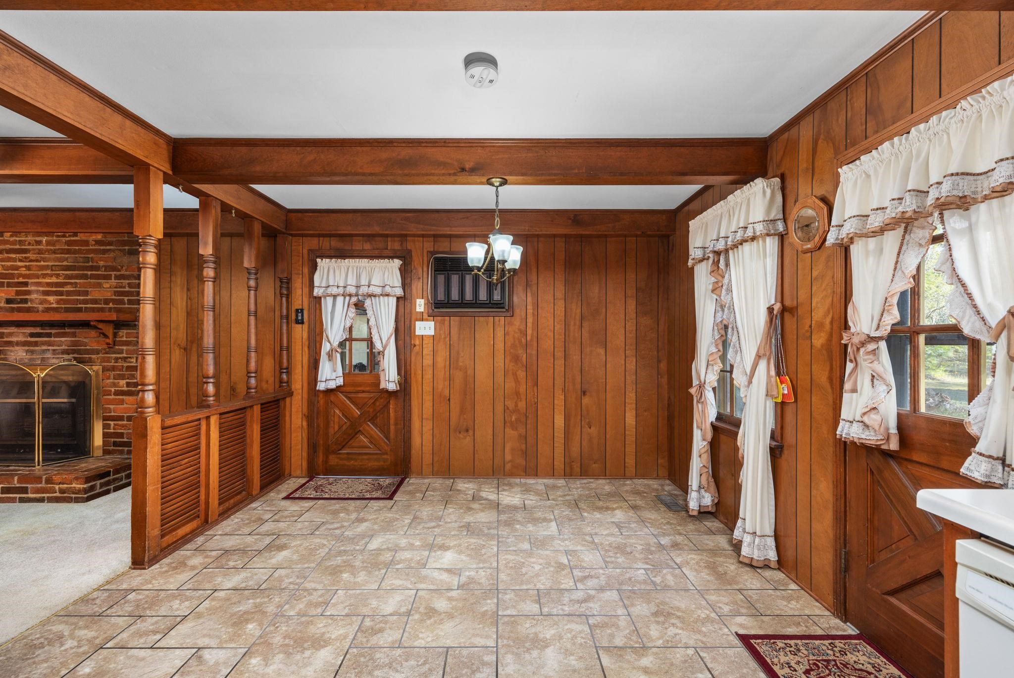 Foyer entrance featuring a fireplace, beam ceiling, an inviting chandelier, and wooden walls