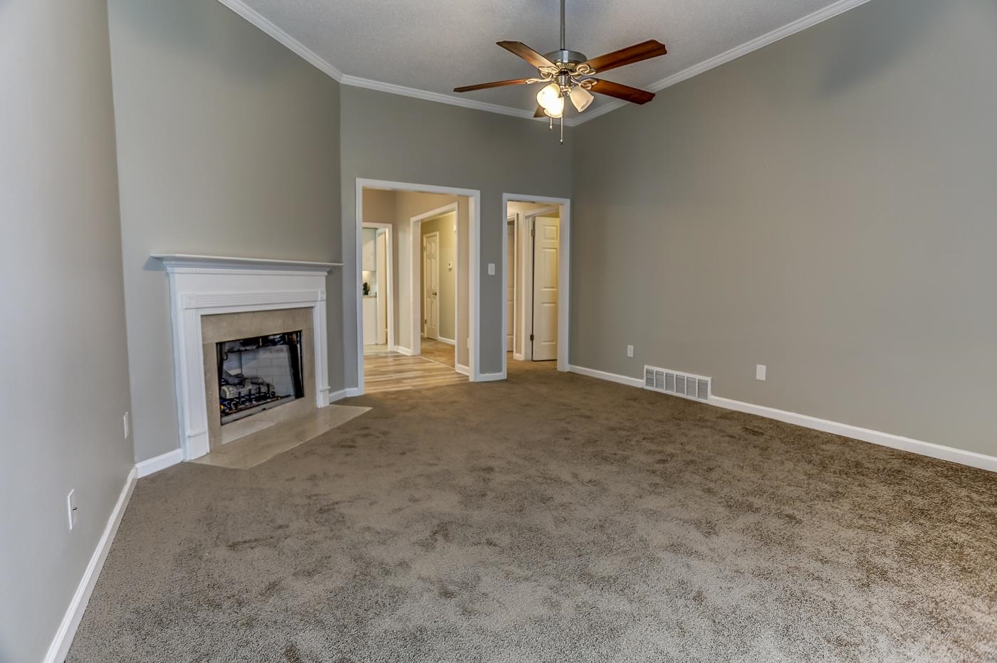 Unfurnished living room with light colored carpet, ceiling fan, and crown molding