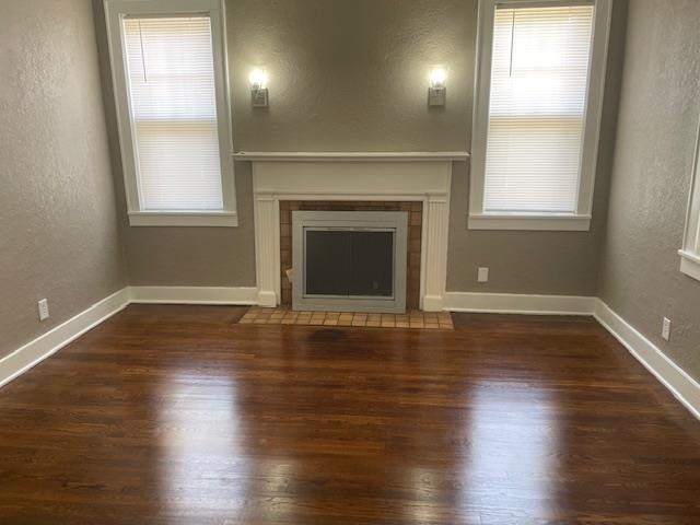 Unfurnished living room featuring a fireplace, a healthy amount of sunlight, and dark wood-type flooring