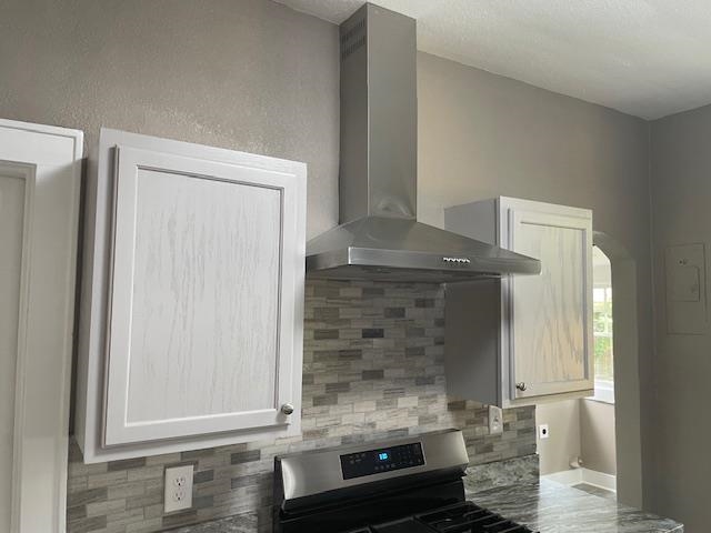 Kitchen featuring backsplash, white cabinets, wall chimney exhaust hood, and stainless steel stove