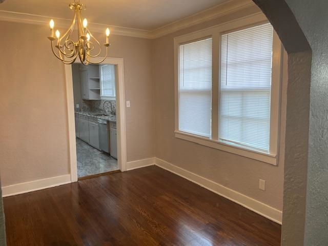 Unfurnished dining area featuring dark hardwood / wood-style floors, a healthy amount of sunlight, ornamental molding, and a chandelier