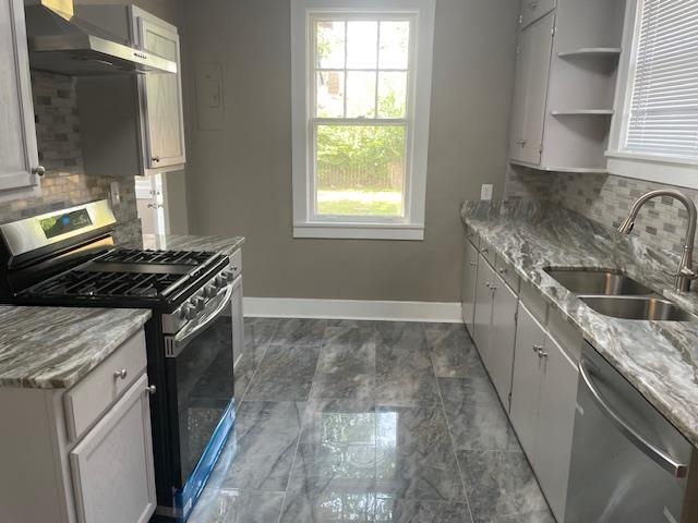 Kitchen featuring backsplash, white cabinets, wall chimney range hood, sink, and appliances with stainless steel finishes