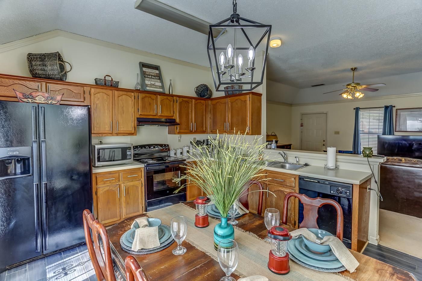 Kitchen featuring black appliances, ceiling fan with notable chandelier, sink, hanging light fixtures, and light wood-type flooring