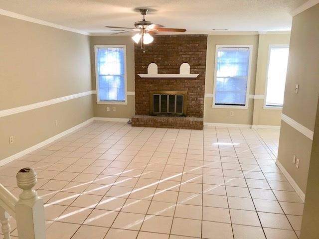 Unfurnished living room with tile patterned floors, a wealth of natural light, ornamental molding, and ceiling fan