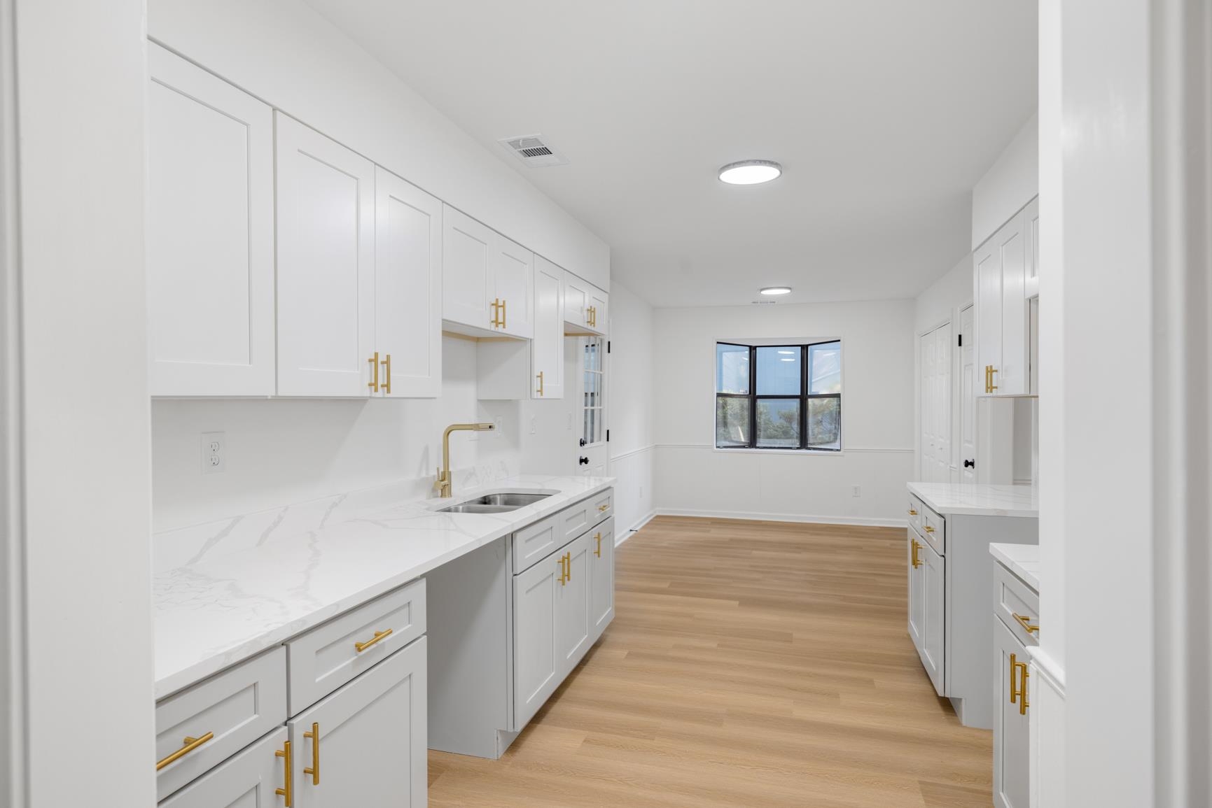 Kitchen featuring light stone counters, light hardwood / wood-style floors, white cabinetry, and sink