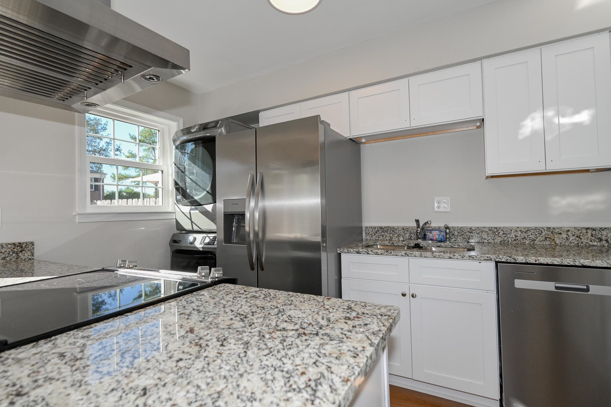 Kitchen featuring light stone countertops, appliances with stainless steel finishes, exhaust hood, hardwood / wood-style flooring, and white cabinetry