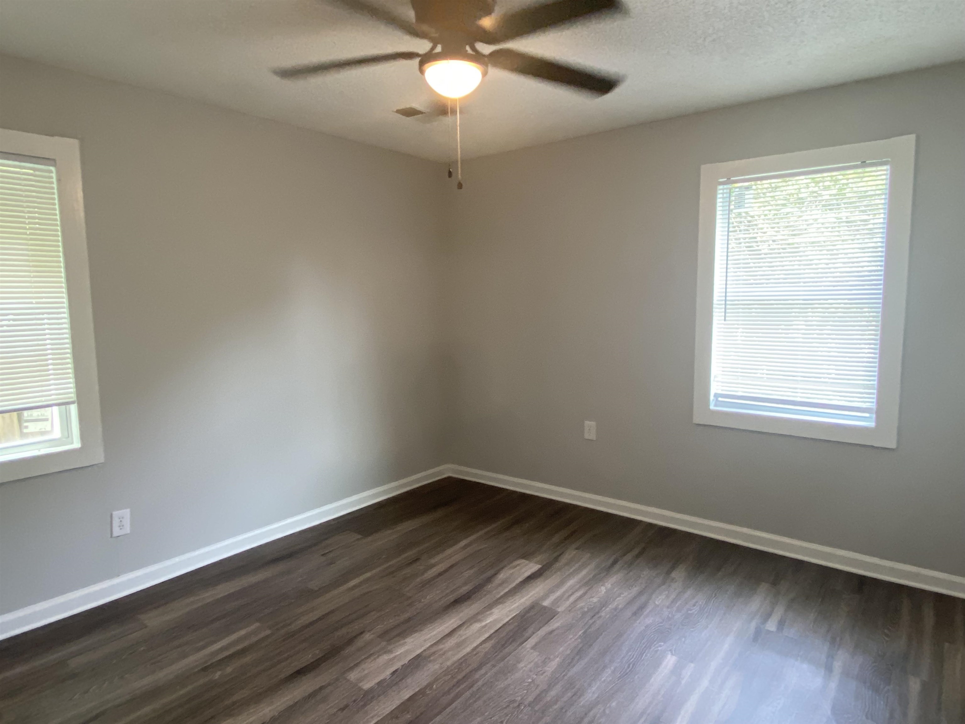 Empty room with ceiling fan, dark wood-type flooring, and a textured ceiling