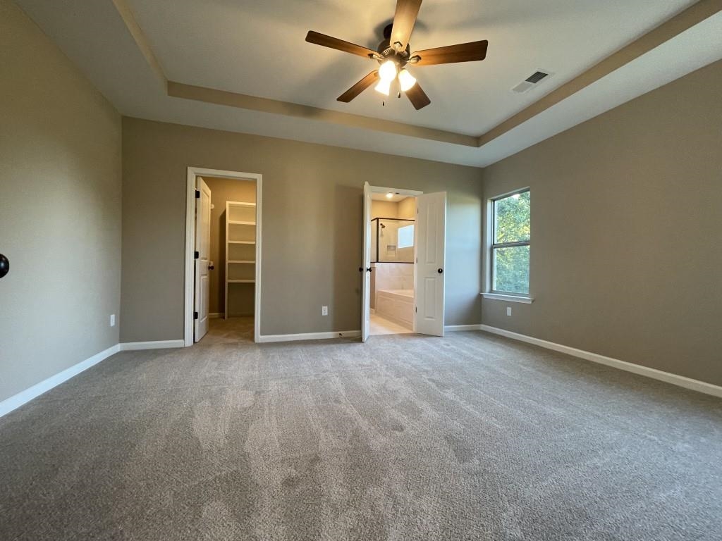 Unfurnished bedroom featuring a walk in closet, carpet flooring, ceiling fan, connected bathroom, and a tray ceiling