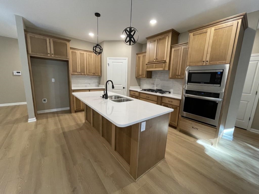 Kitchen with sink, stainless steel appliances, light hardwood / wood-style flooring, backsplash, and a kitchen island with sink