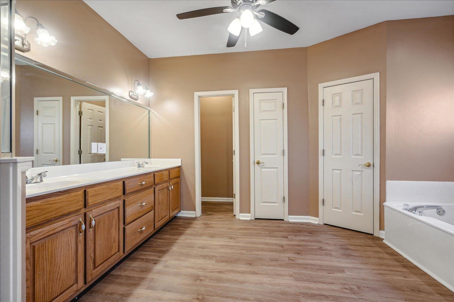 Bathroom with hardwood / wood-style floors, vanity, ceiling fan, and a washtub