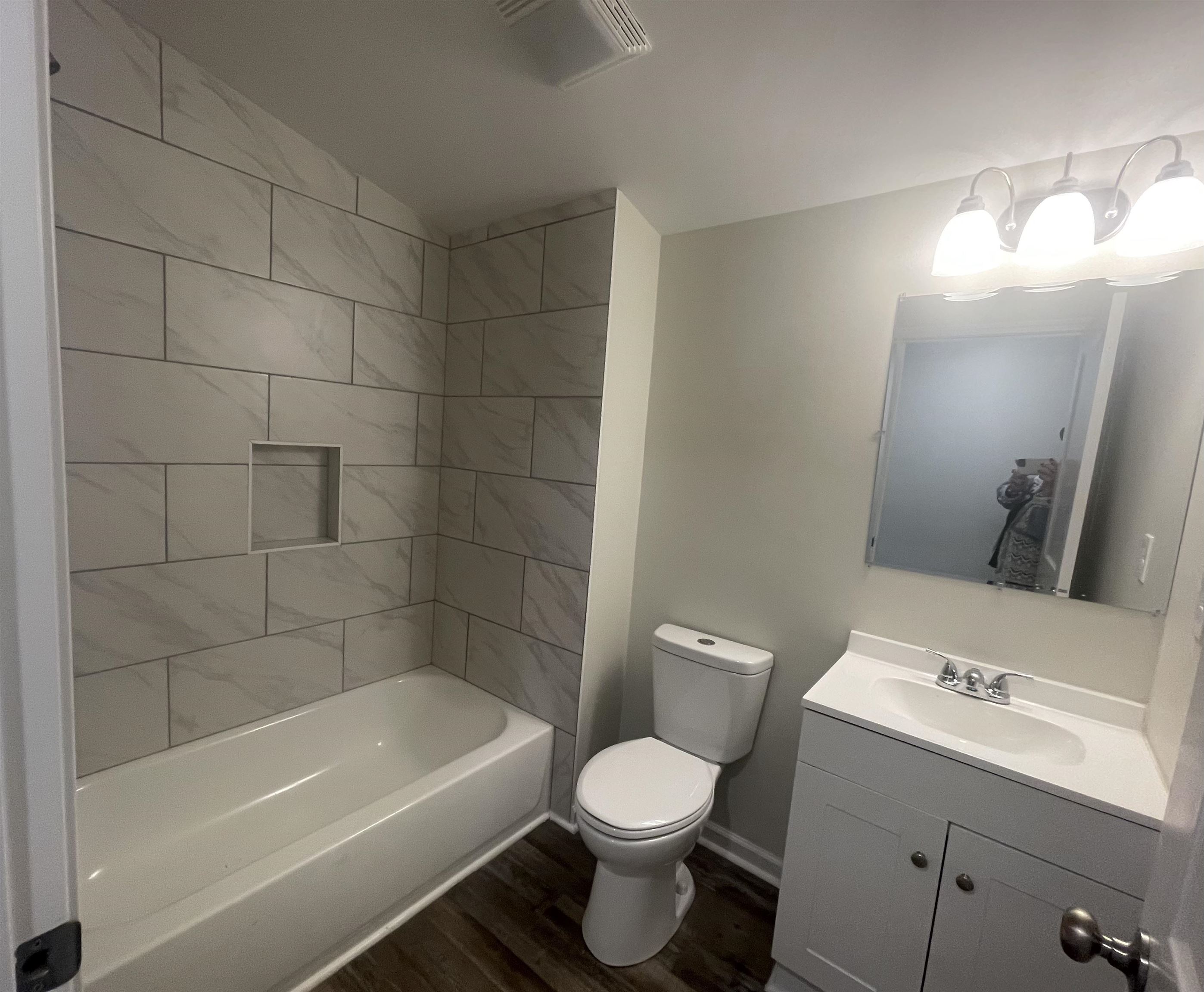 Full bathroom with vanity, lofted ceiling, tiled shower / bath, hardwood / wood-style flooring, and toilet