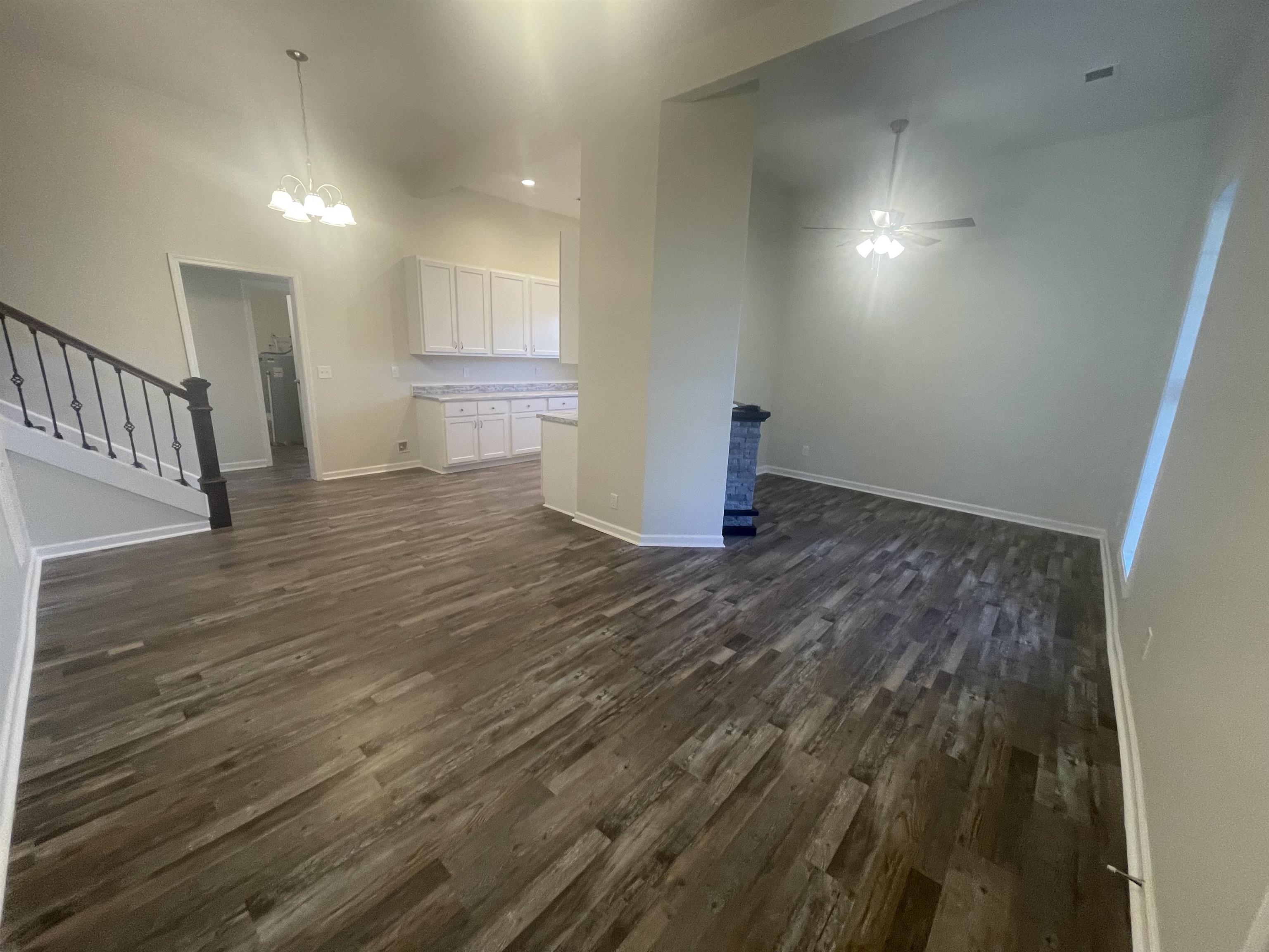 Unfurnished living room featuring ceiling fan with notable chandelier and dark hardwood / wood-style floors